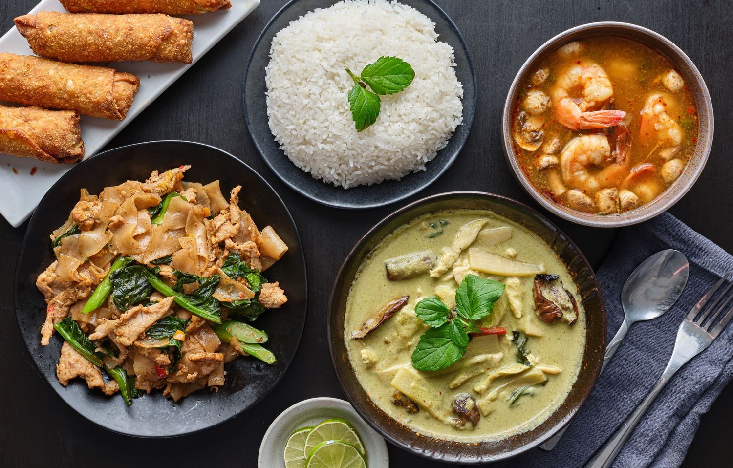 Asian curry dishes with rice and spring rolls served in dark bowls.