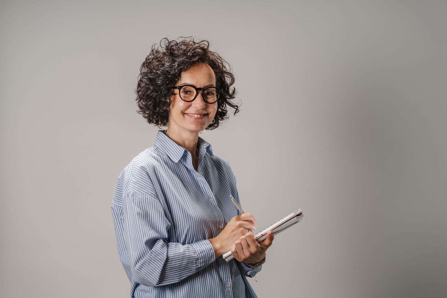 Person in casual blue shirt using mobile device against grey background.