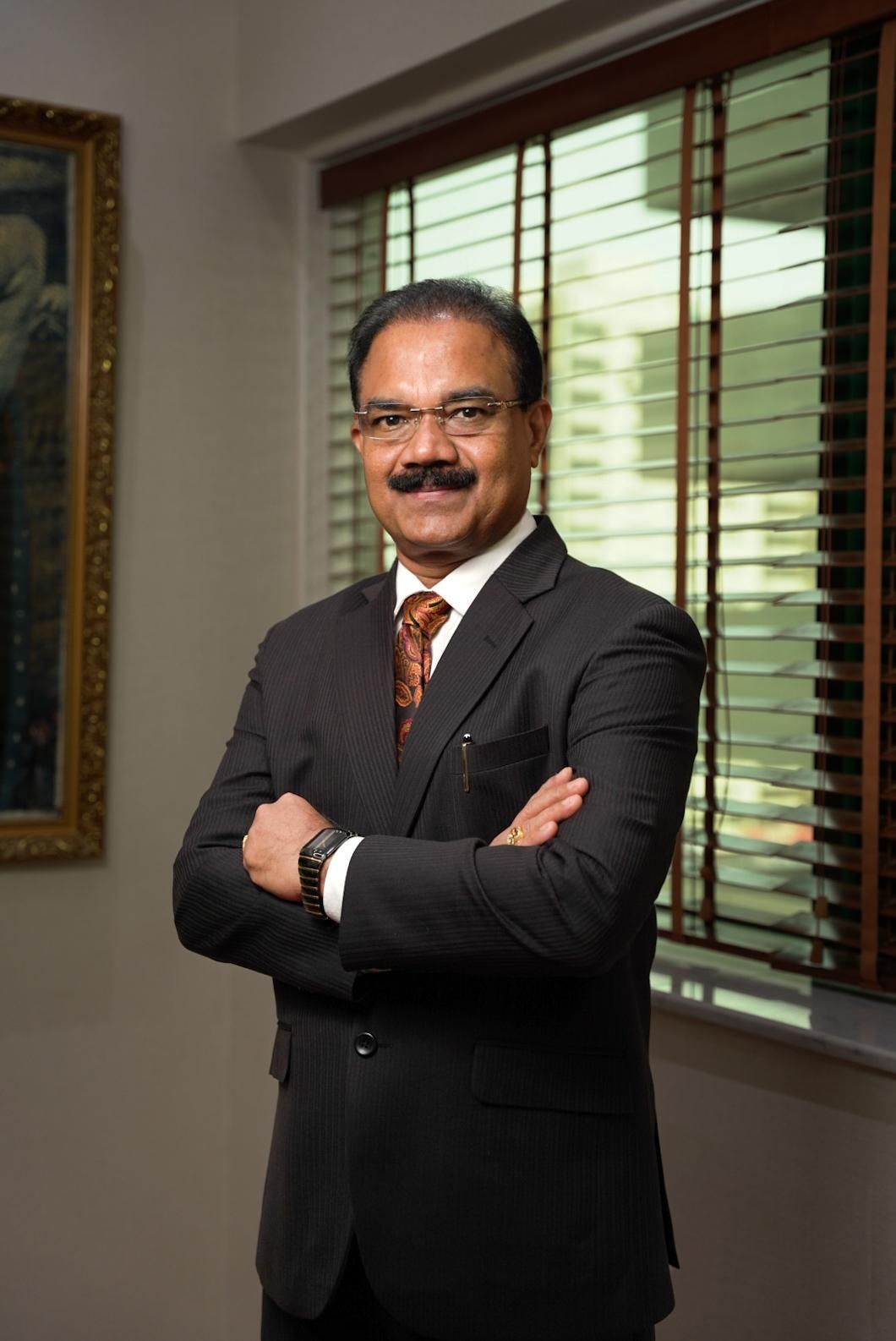 Professional portrait series showing a person in a dark business suit posing with crossed arms against a light interior wall.