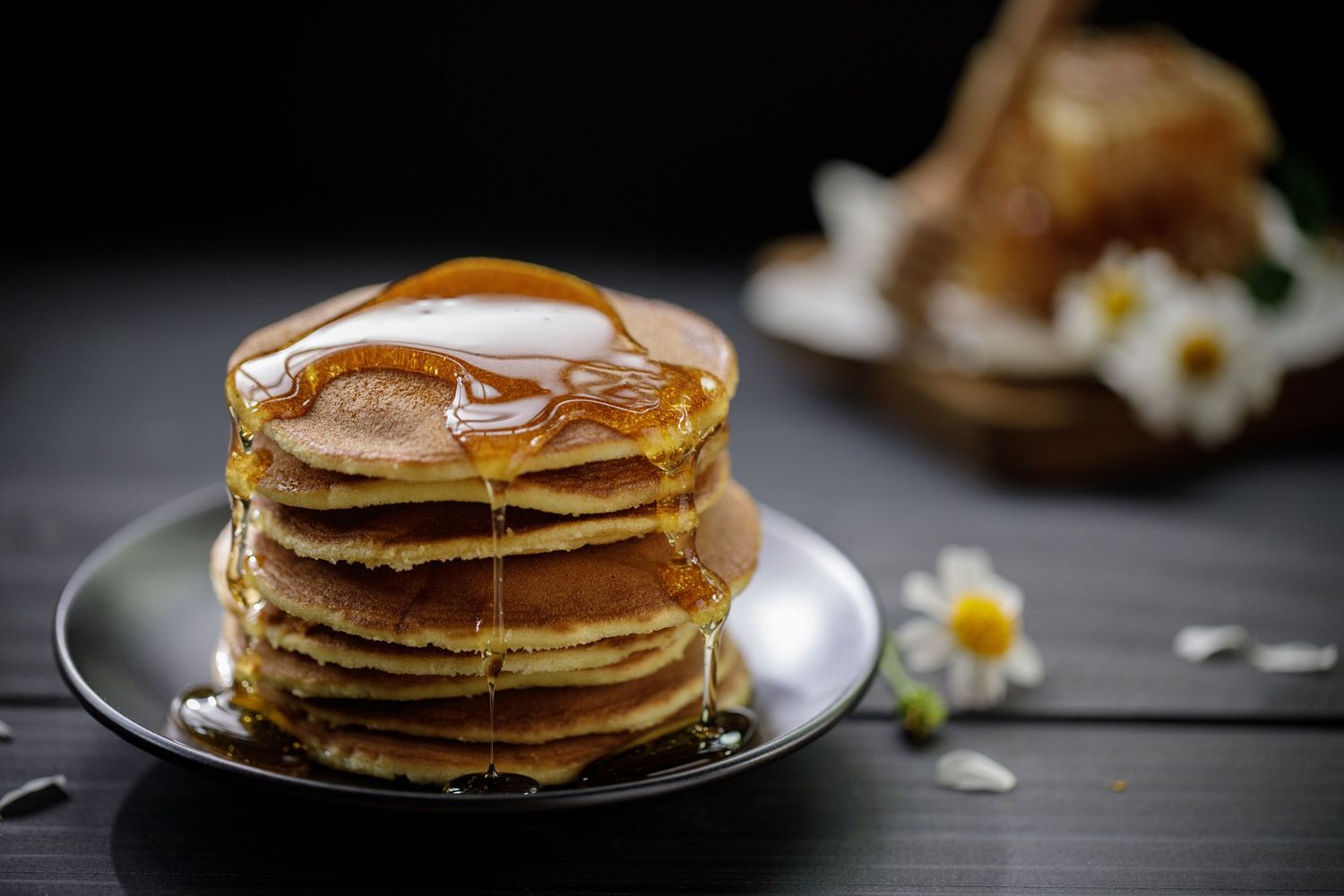 Stack of golden pancakes with syrup dripping down on a dark surface.