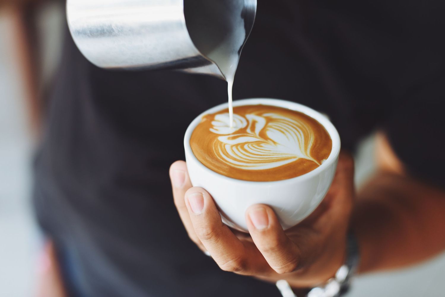 Latte art being poured into white coffee cup creating heart design.