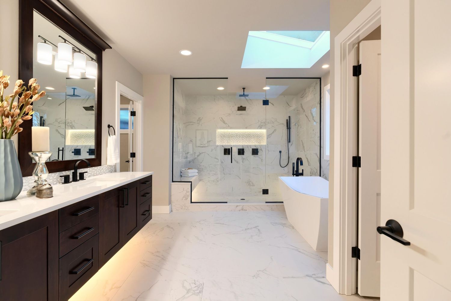 Luxurious modern bathroom with marble floors, glass shower enclosure and dark wood vanity.
