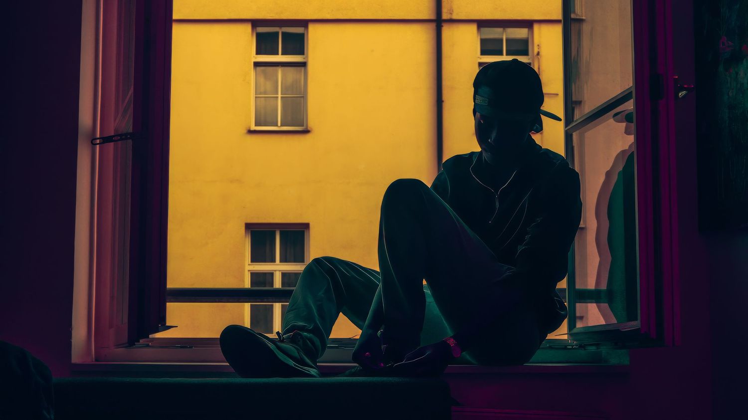 Silhouette sitting in window frame against bright yellow building exterior.