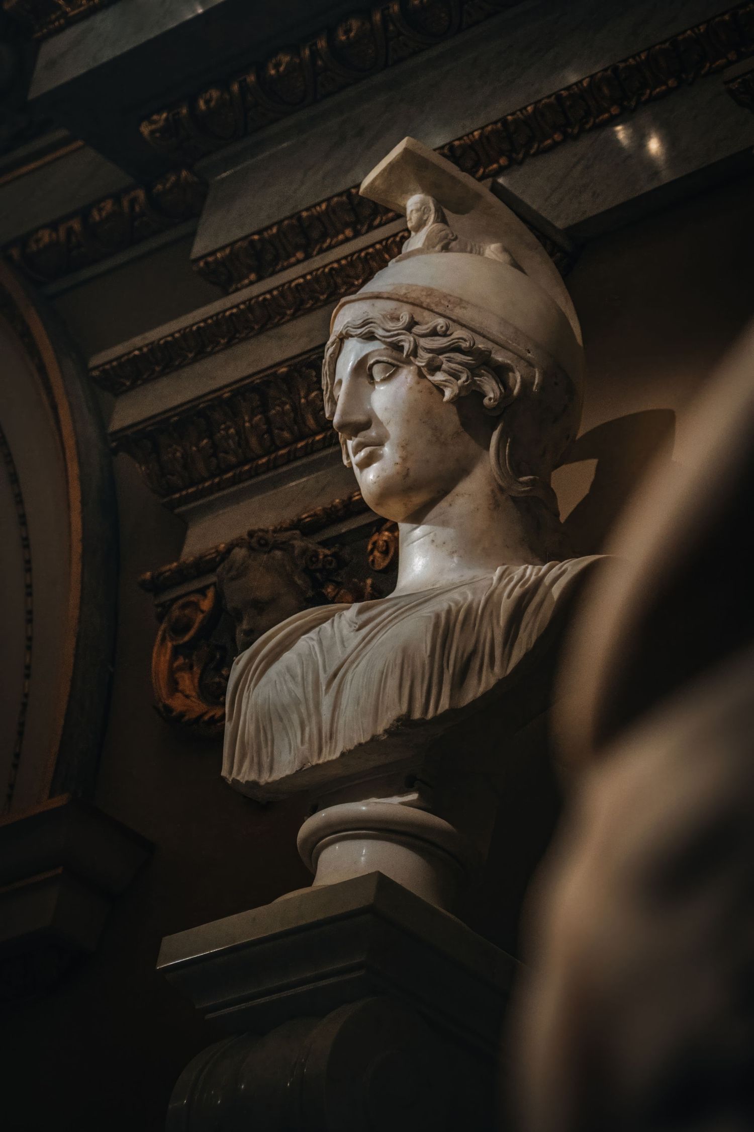 Classical marble bust sculpture wearing helmet photographed in dramatic lighting.