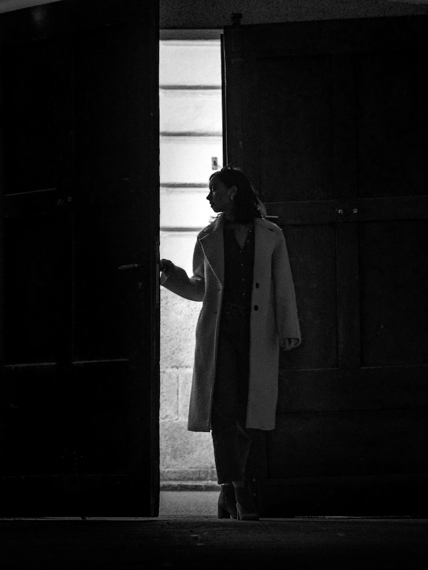 High contrast black and white photo of figure silhouetted against bright window.