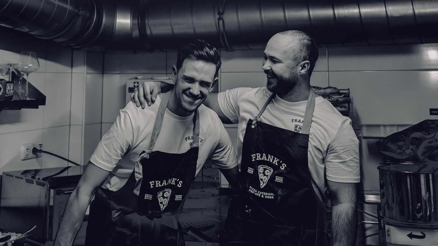 Two people in matching aprons sharing a joyful moment in a kitchen setting.