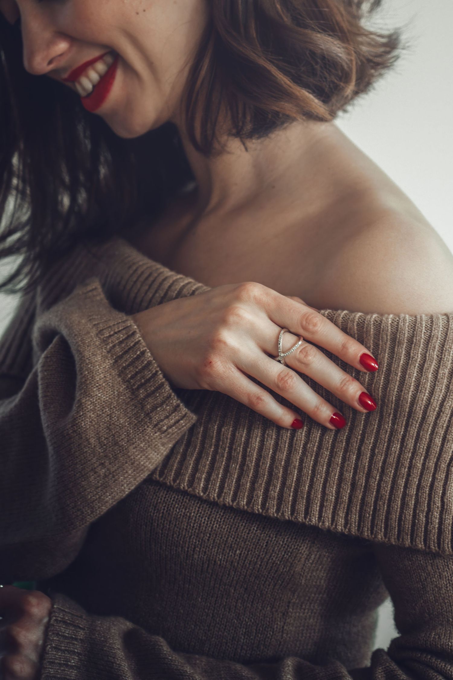 Close-up of hand with red nails and ring touching brown knit sweater.