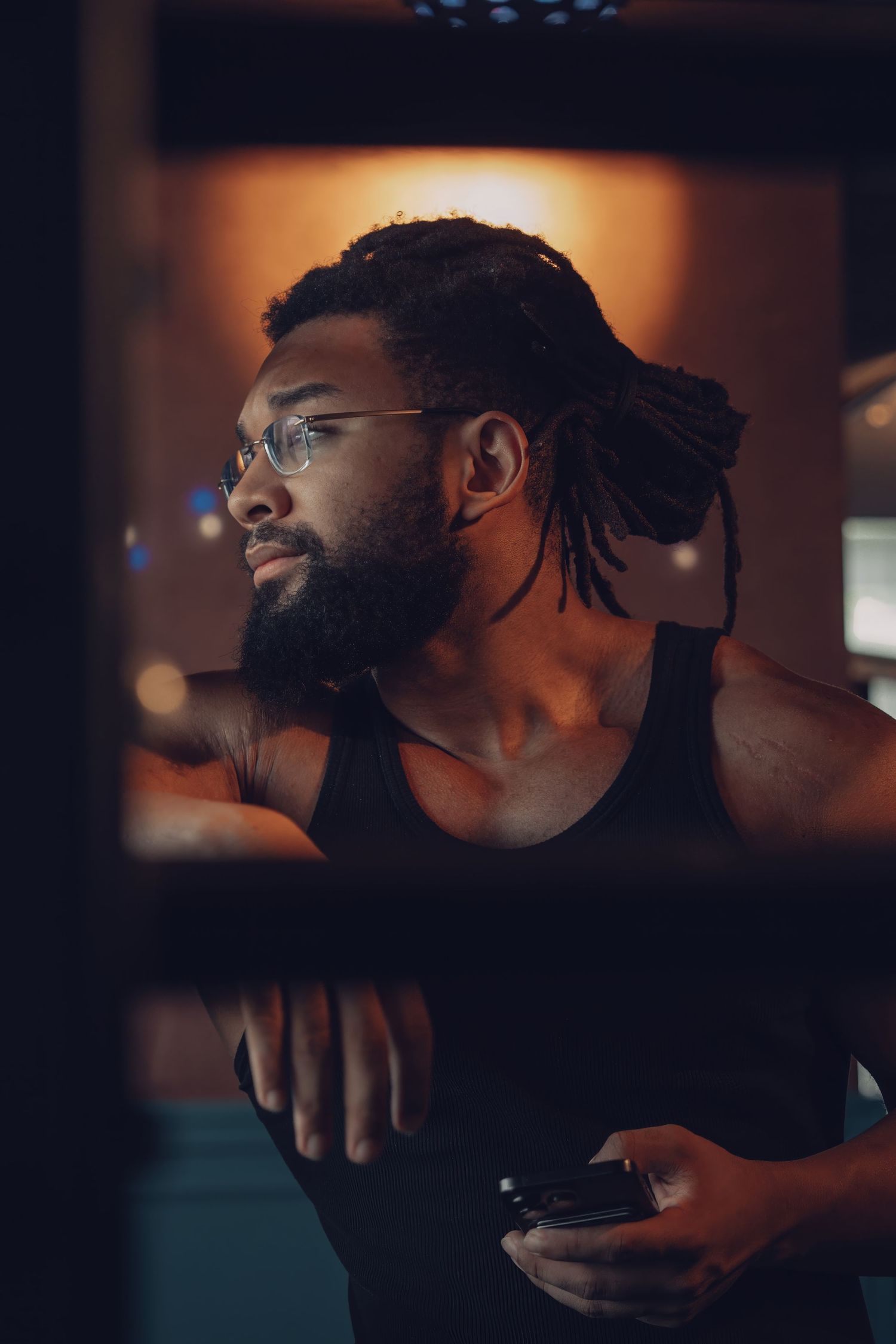 Person in a dark tank top looking thoughtfully to the side in warm ambient lighting.