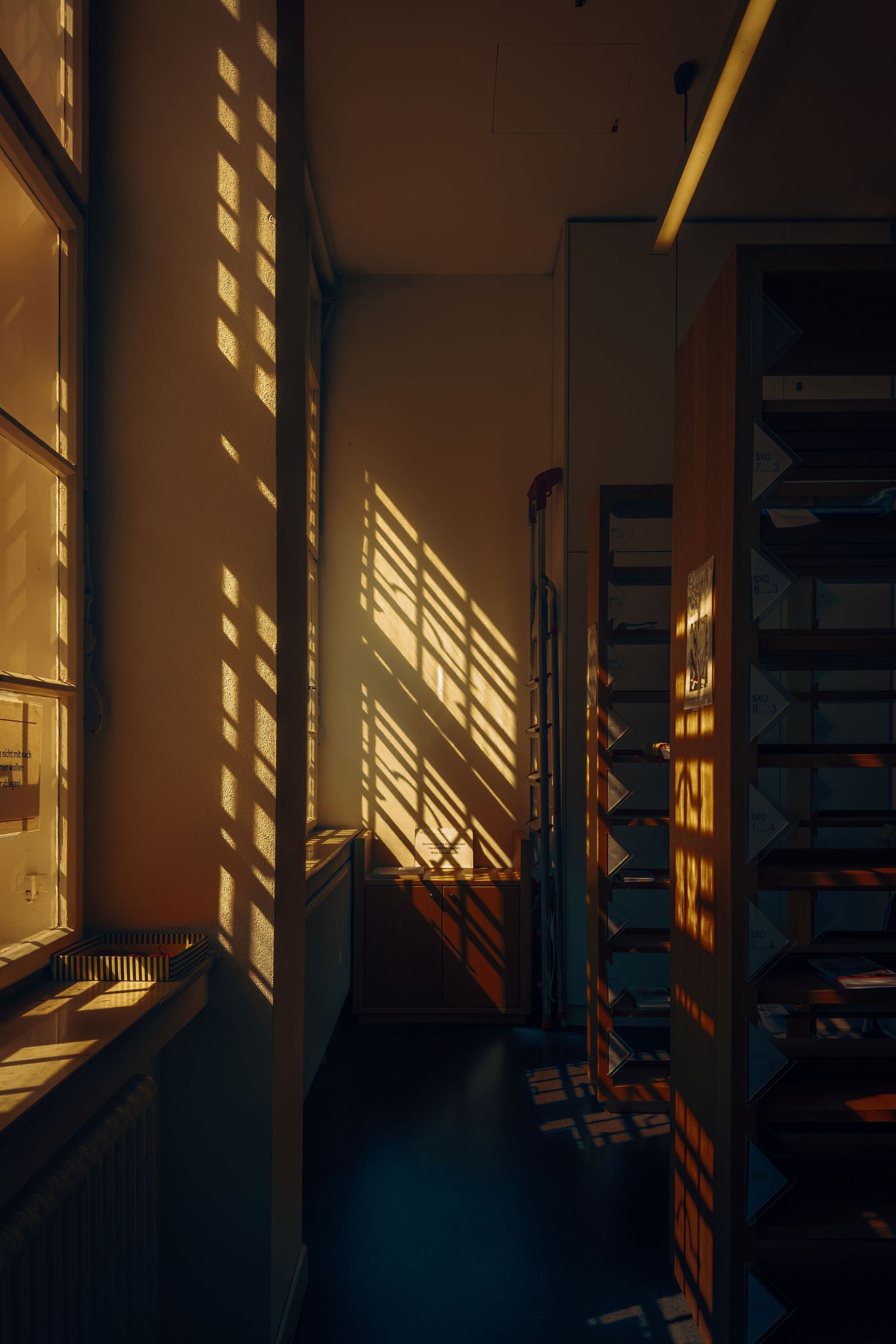 Dramatic shadows from sunlight streaming through windows create geometric patterns on an interior wall.
