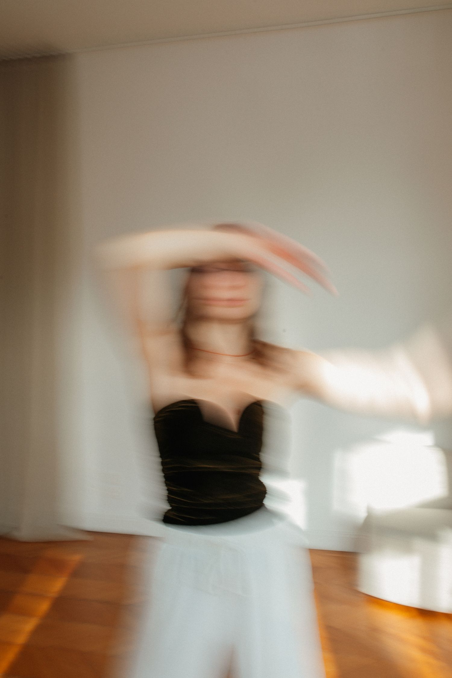 Abstract motion blur photograph shows a figure in black clothing spinning against a white wall and wooden floor.