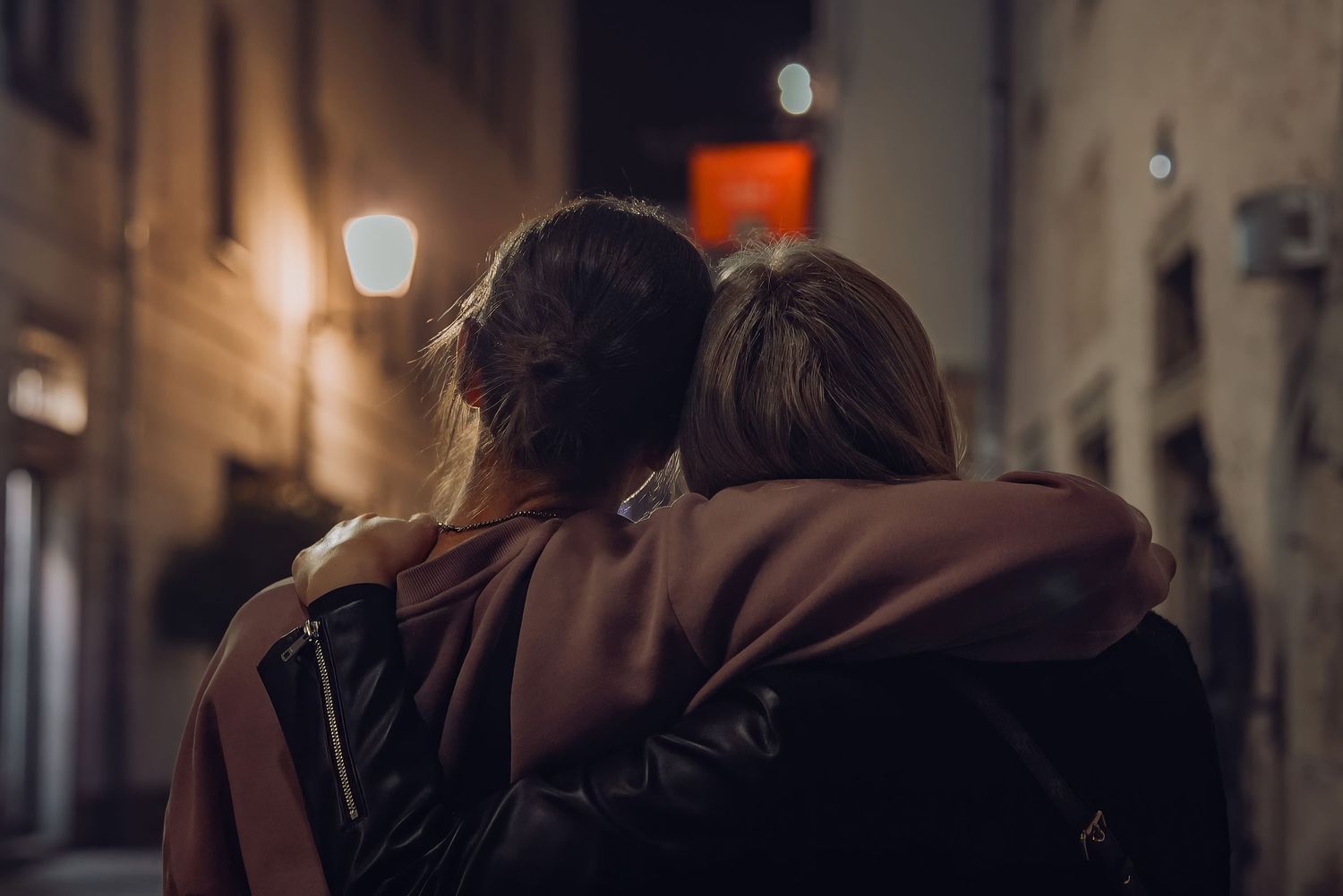 Couple embracing in warm coats on dimly lit street at night.