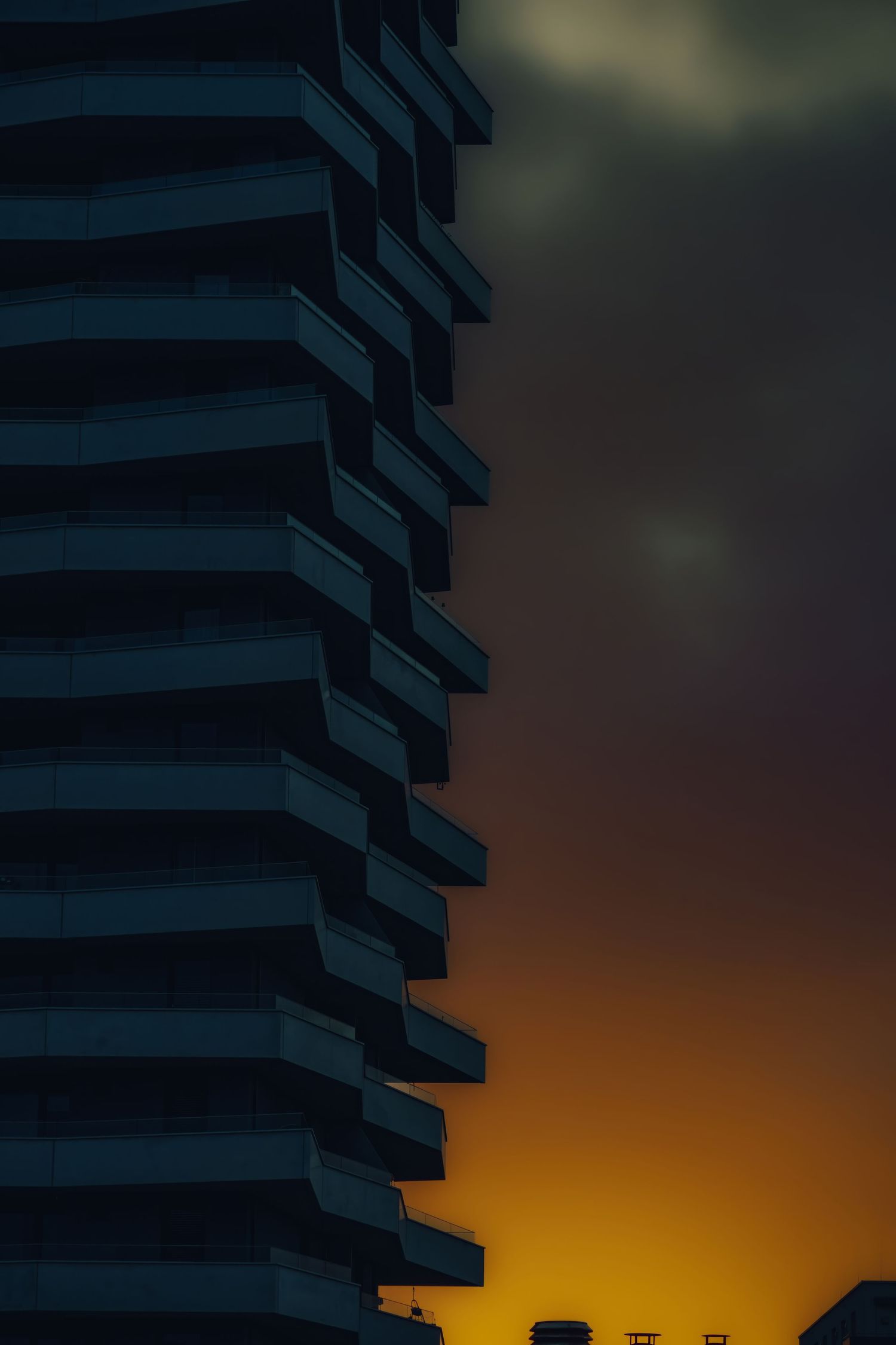 Modern apartment building silhouetted against vibrant orange and purple sunset sky.