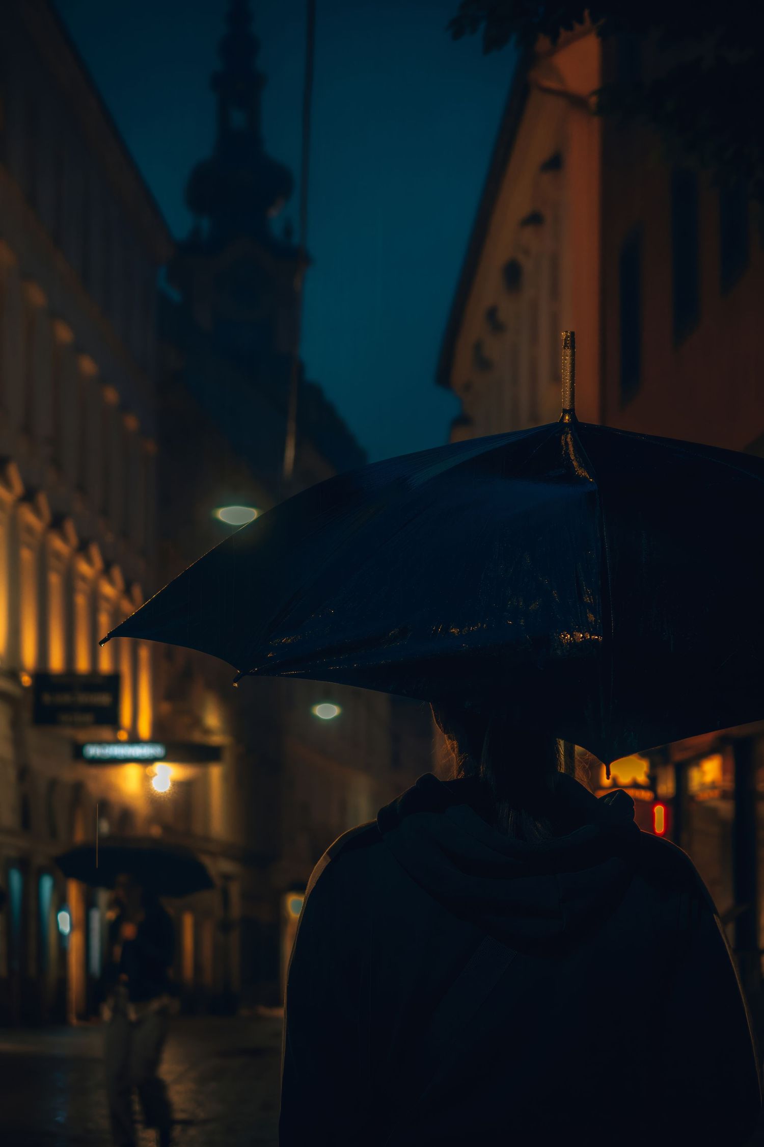 Dark city street at night with glowing streetlights and umbrellas casting shadows.