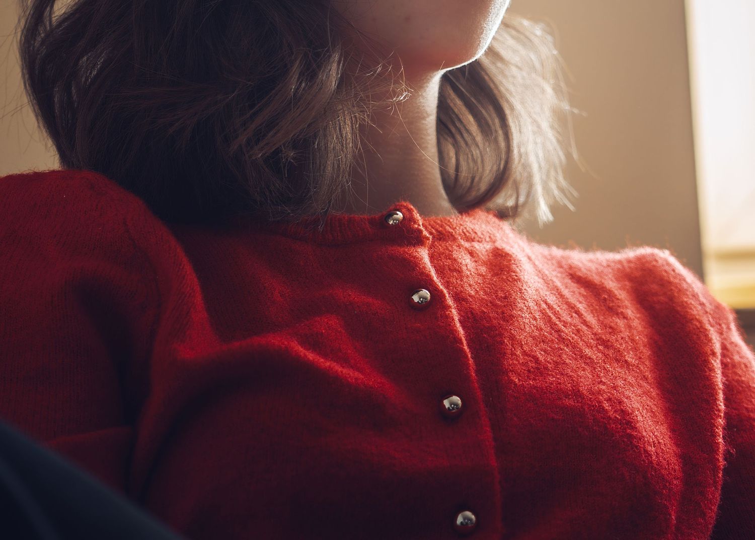 Person wearing a red buttoned cardigan sweater in soft natural lighting.