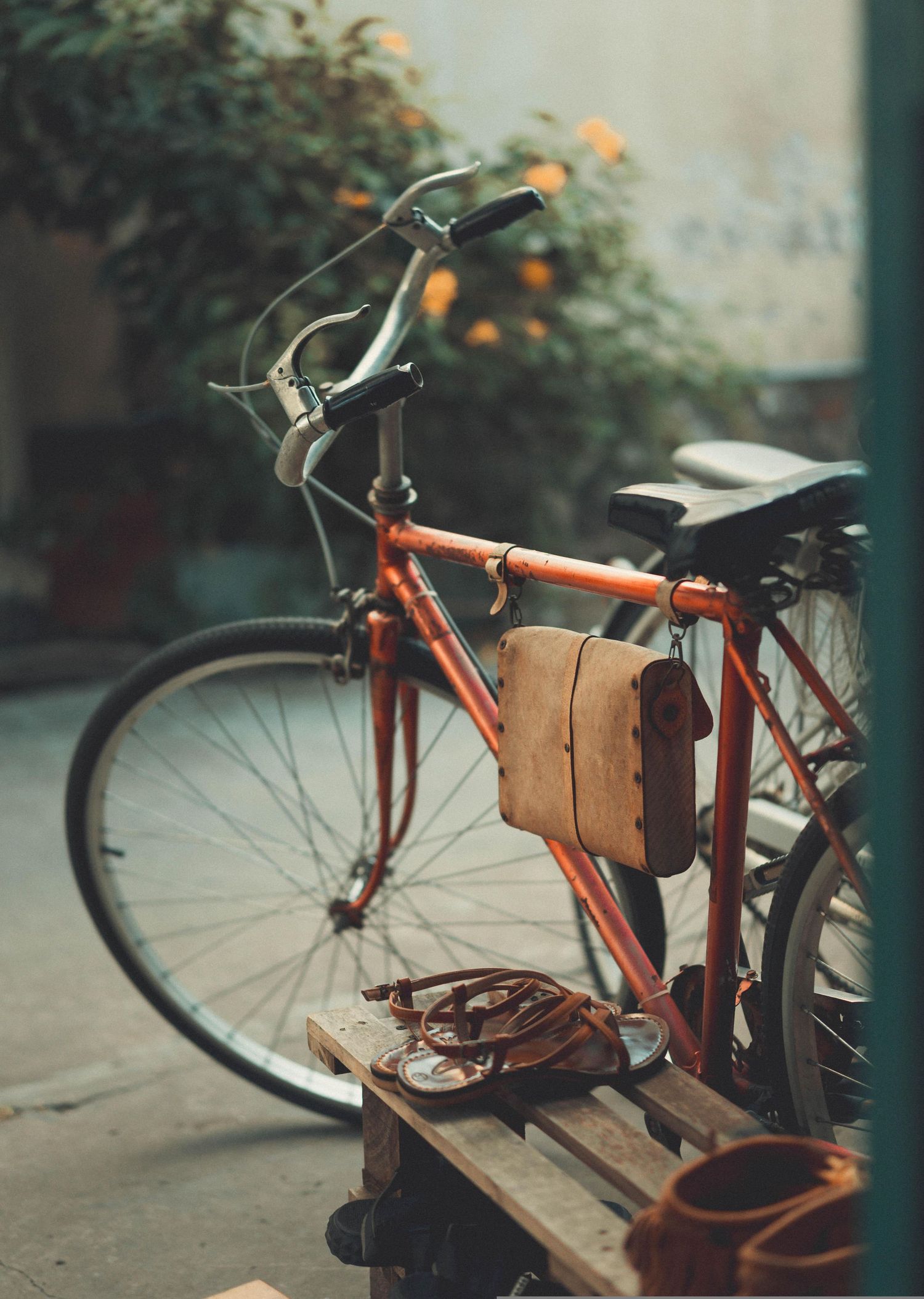 A vintage orange bicycle with brown leather accessories parked against a blurred background outdoors.