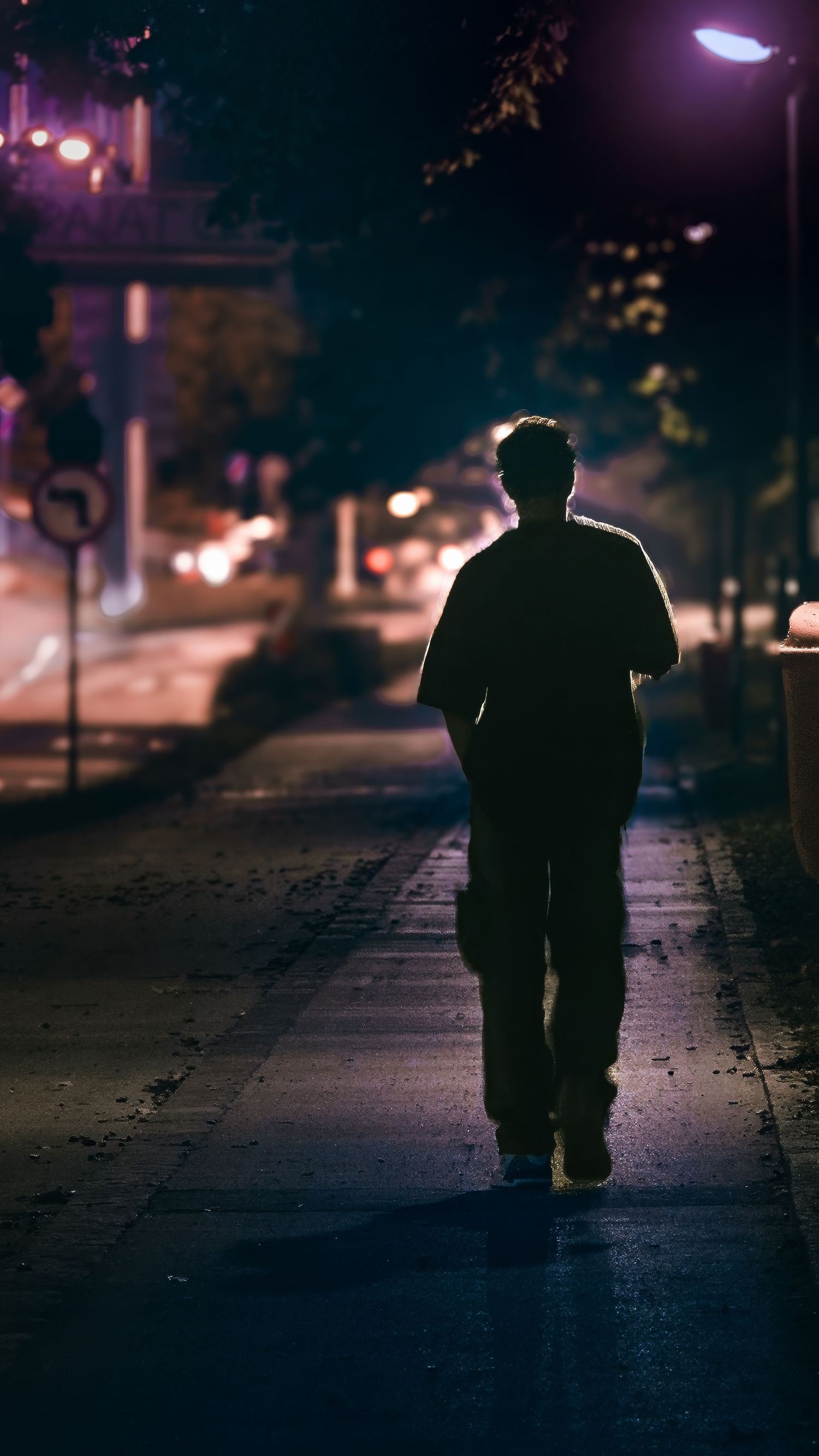 Silhouette of a person walking alone on a dark street at night with purple lighting.
