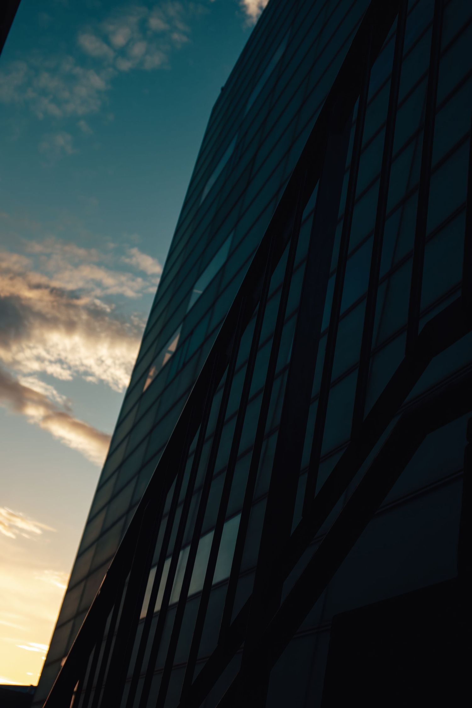 Modern glass office building facade reflecting sunset sky and clouds.