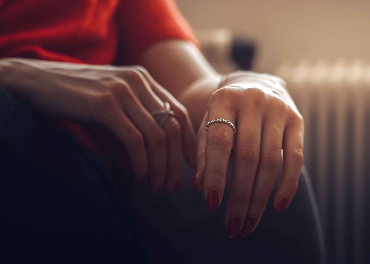 Hands resting on lap showing delicate ring jewelry with atmospheric lighting.