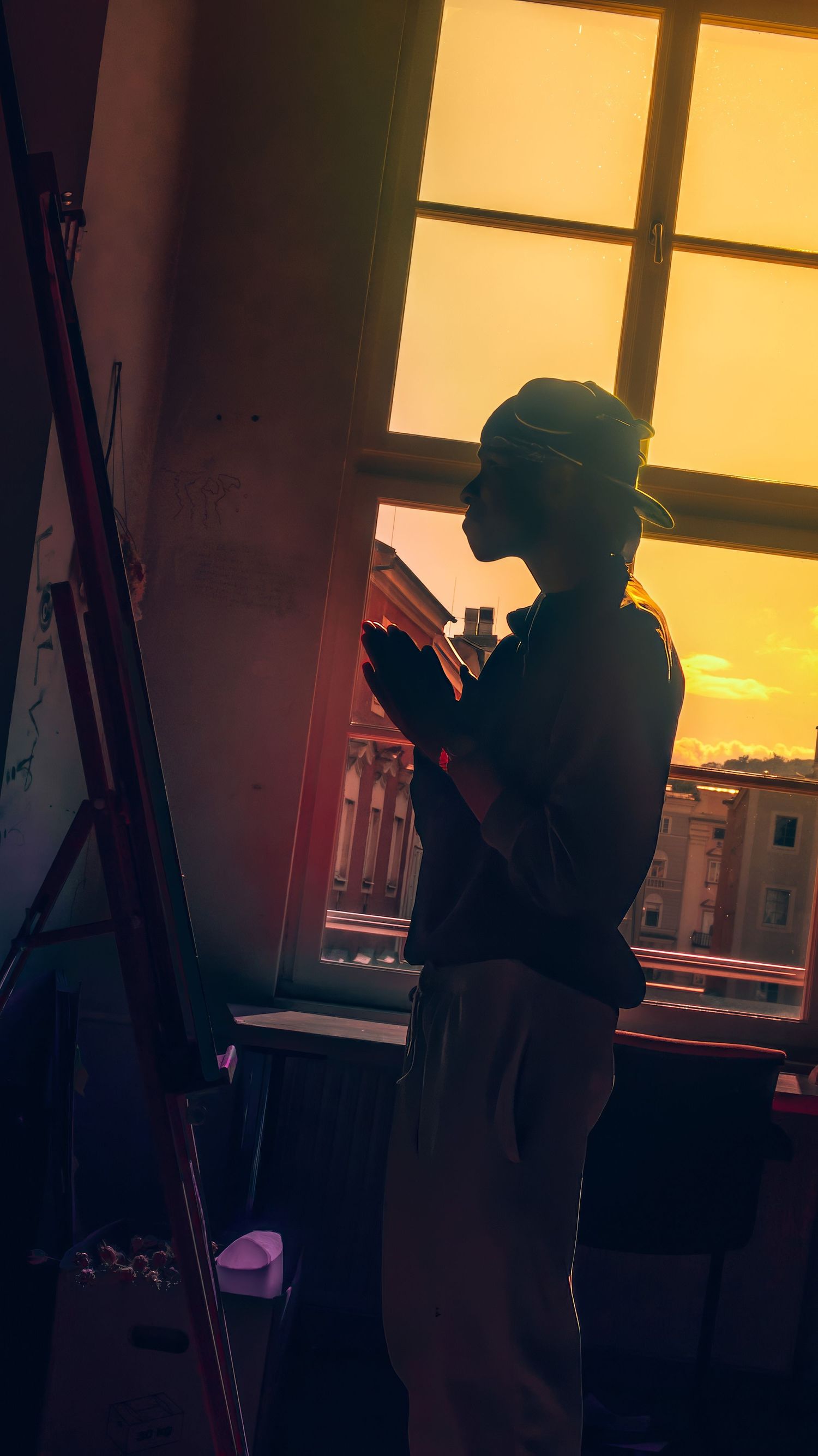 Silhouette of a person looking at phone by window during golden sunset hour.