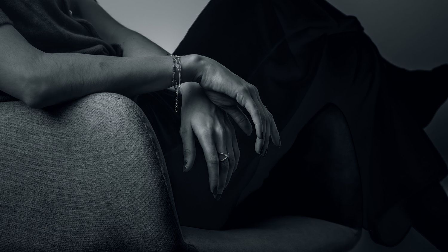 Artistic black and white photograph showing hands resting on dark fabric in moody lighting.
