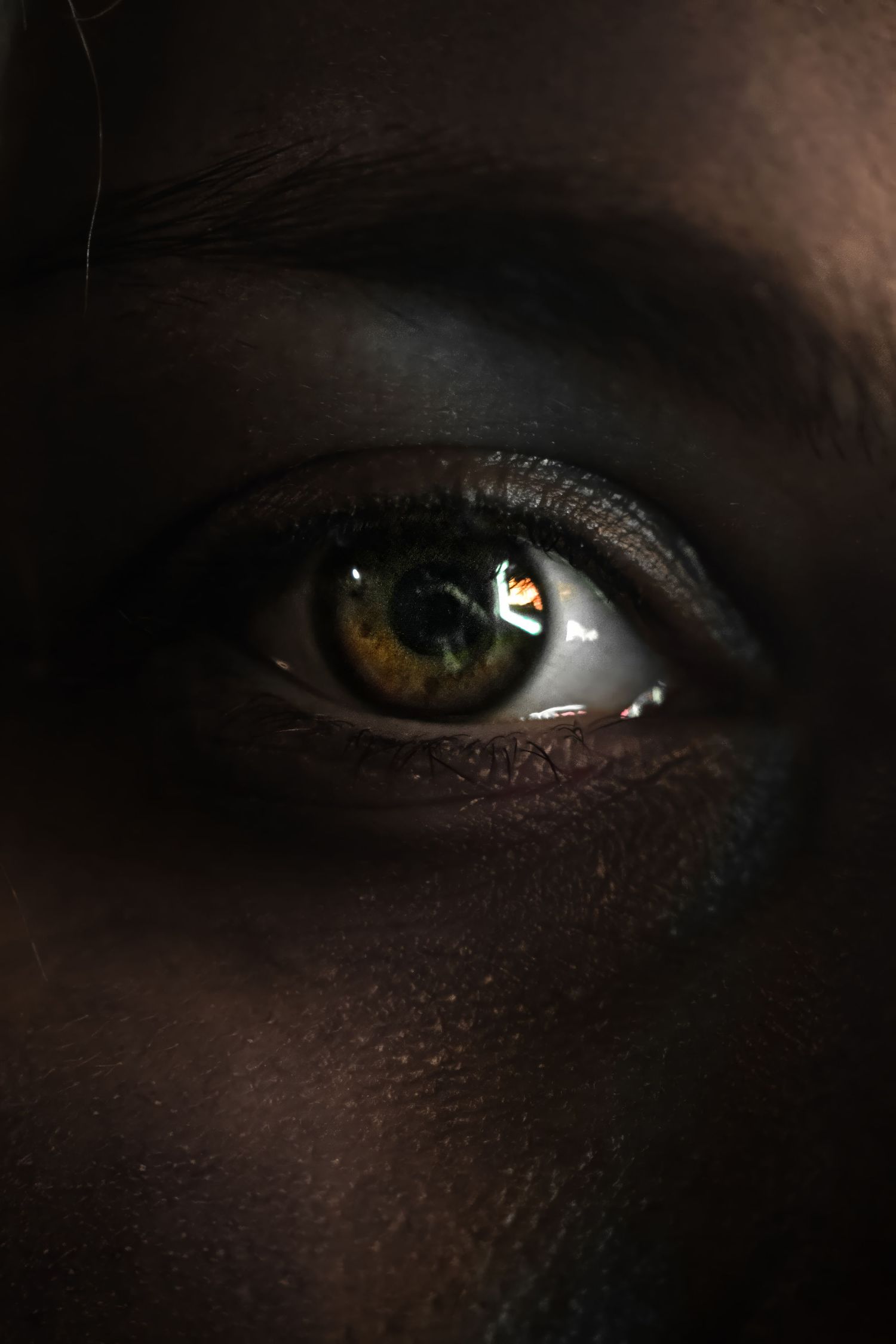 Extreme close-up of an eye with amber iris in dramatic dark lighting.