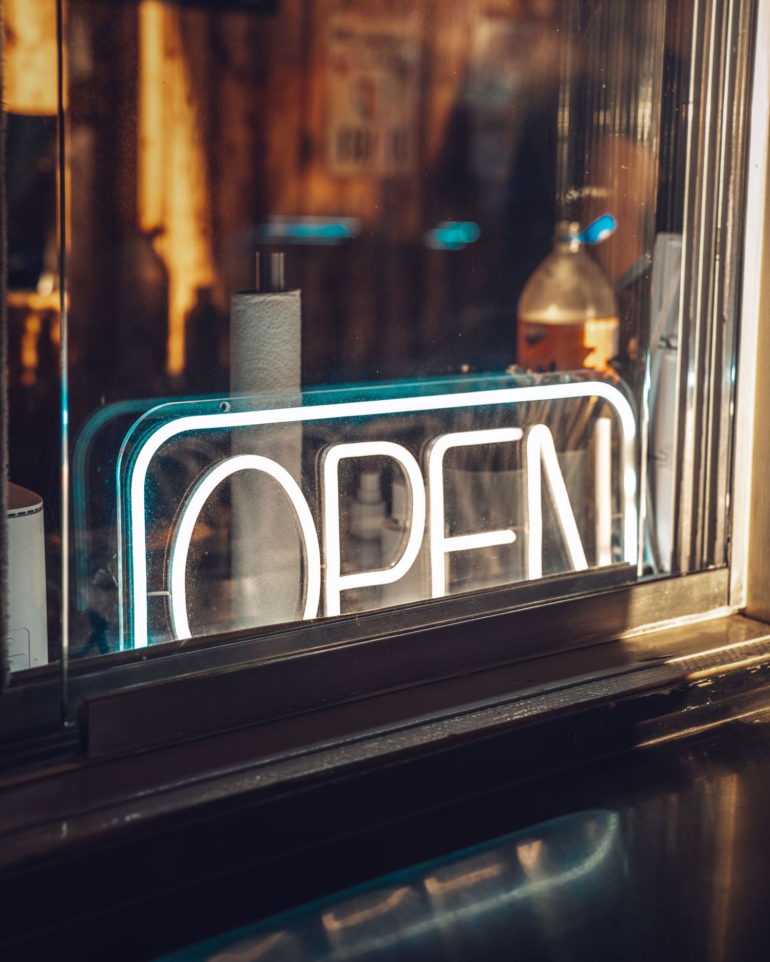 Neon letters glowing through a window at dusk create a moody urban atmosphere.