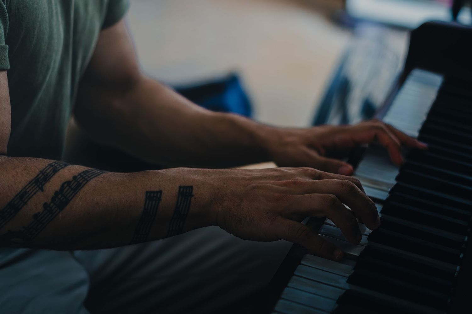 Tattooed hands playing piano keys in moody lighting.