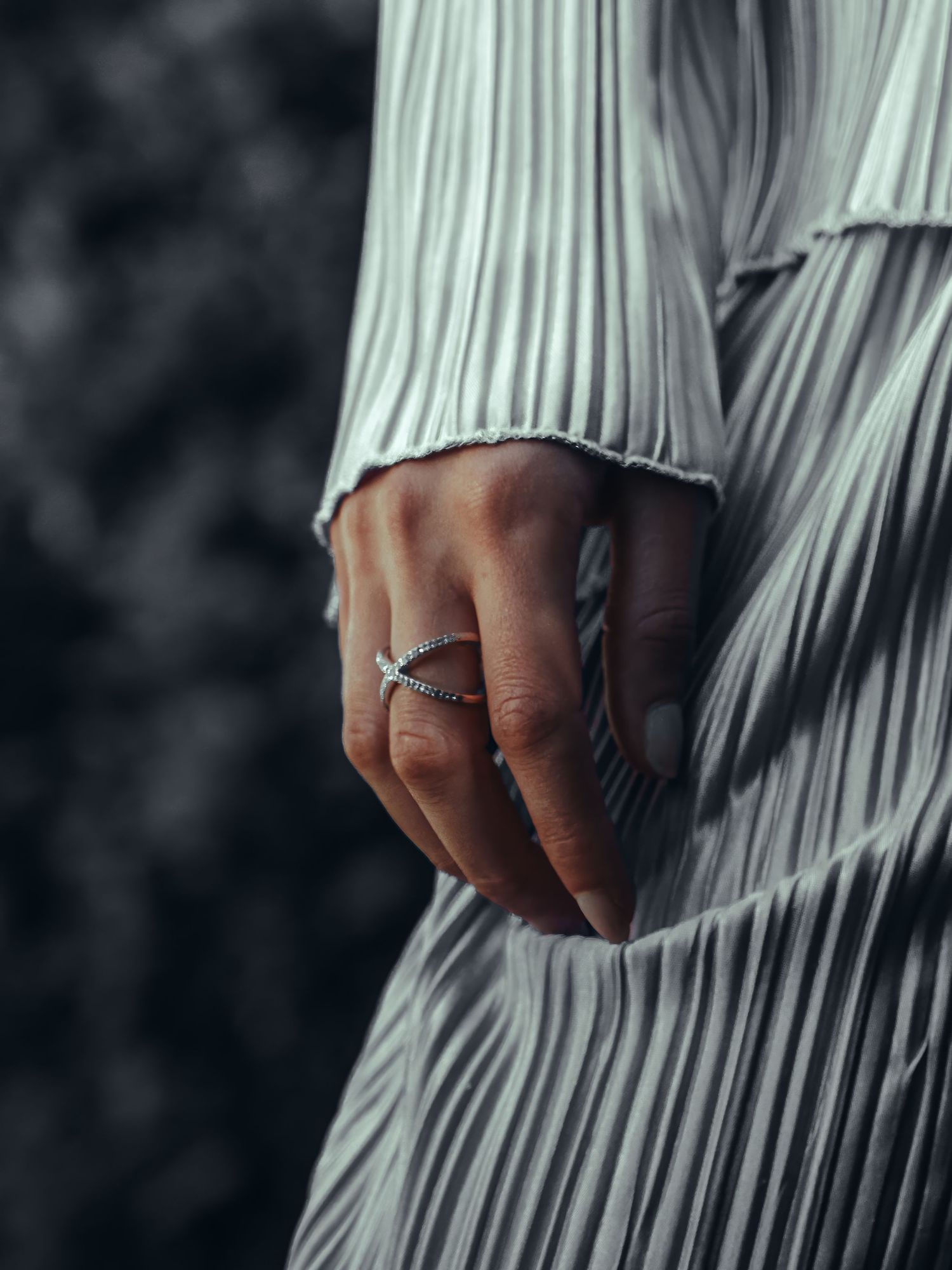 Close-up of hand wearing ring against pleated white fabric.