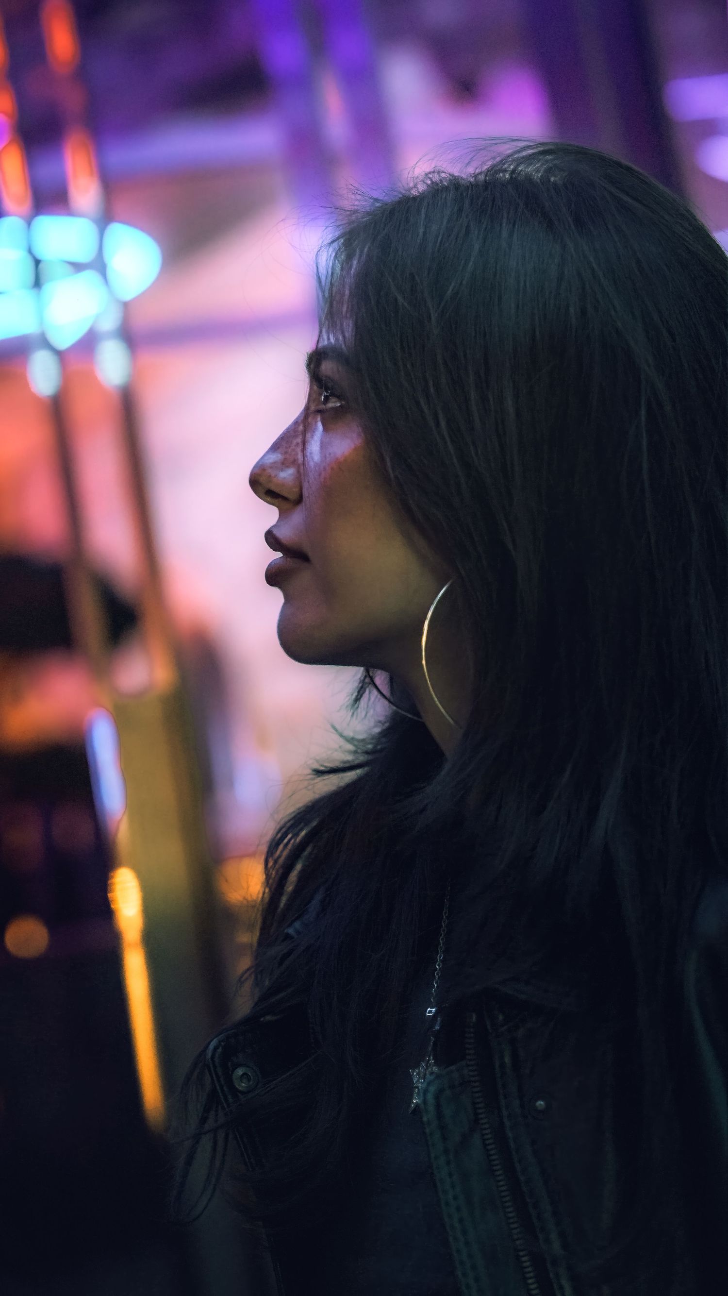 Side profiles silhouetted against neon lights in dark moody nighttime atmosphere with purple and blue hues.