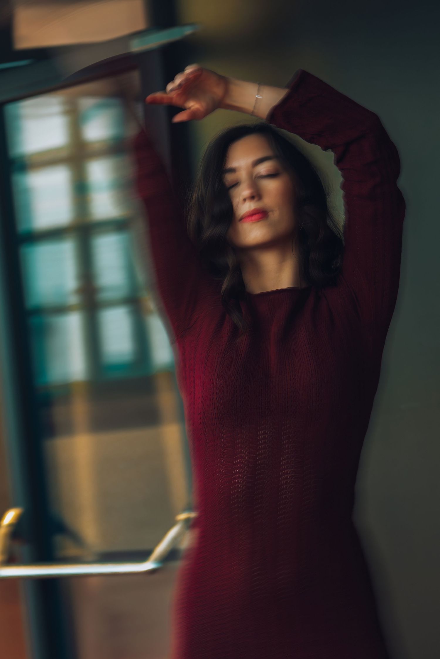 Artistic portrait in burgundy sweater with dramatic motion blur against moody lighting and teal background.