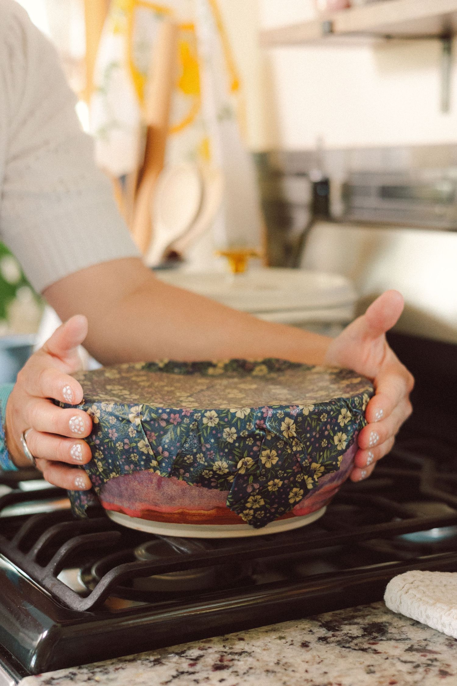 Hands placing a dark-colored pie with speckled crust onto a stovetop burner for cooking.