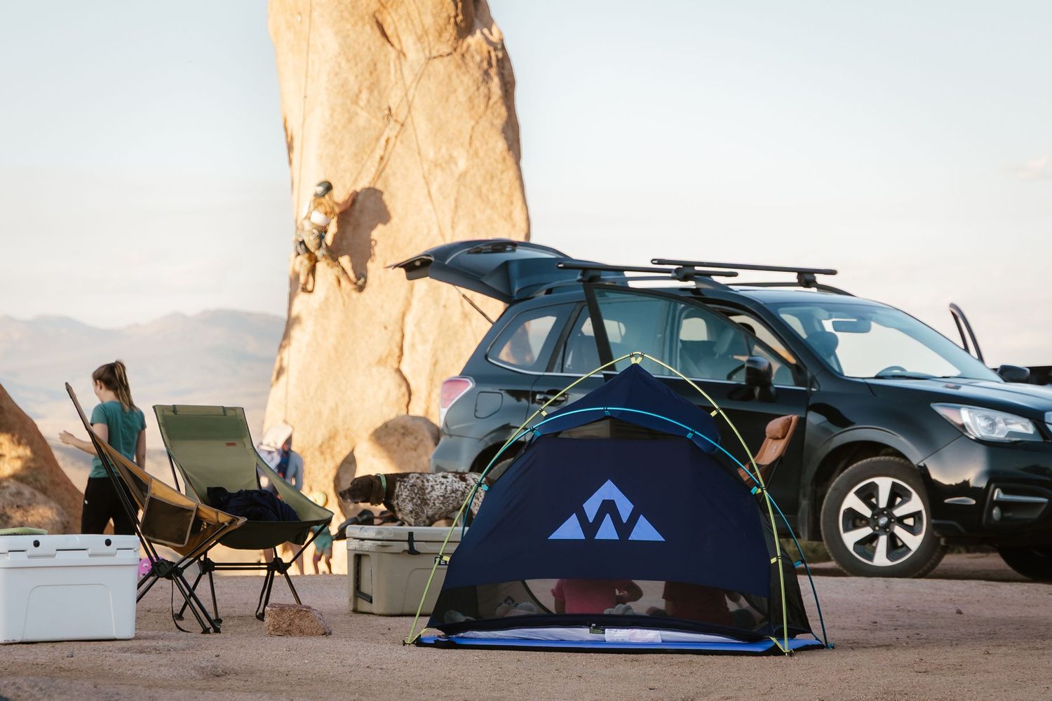 Cars and camping tents set up at a scenic desert campsite with towering rock formations in the background.
