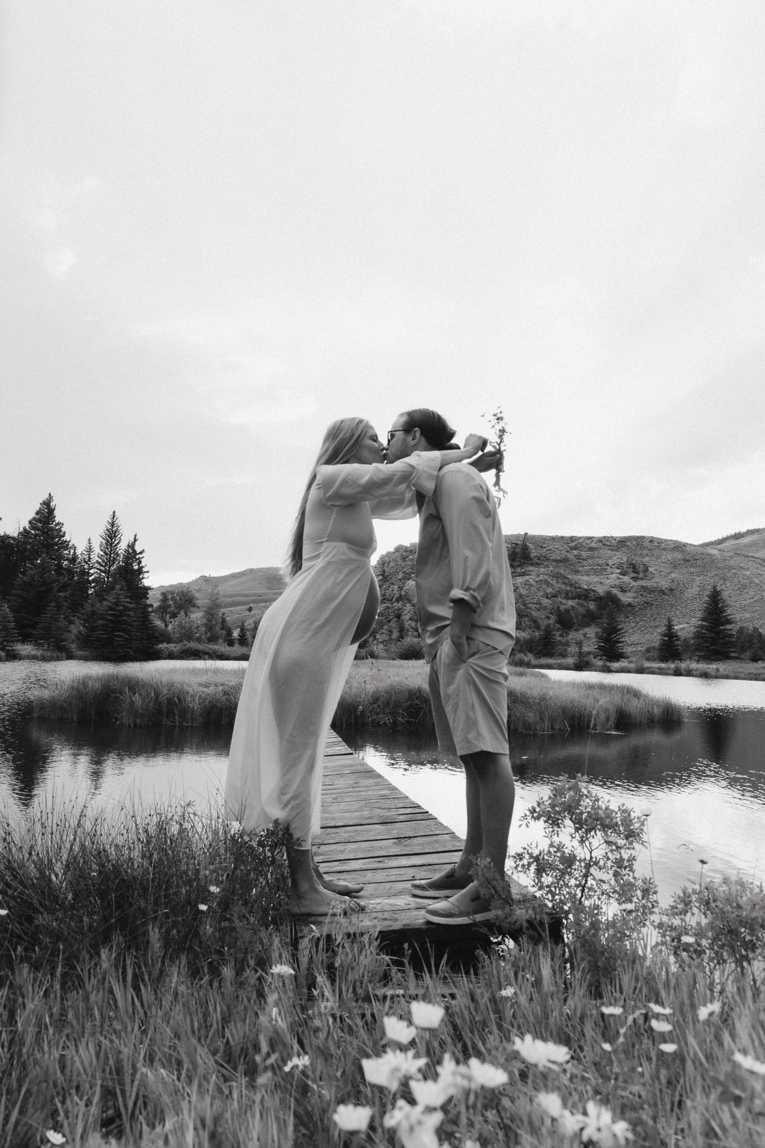Maternity photography session in Crested Butte, Colorado kissing with wildflowers and water.
