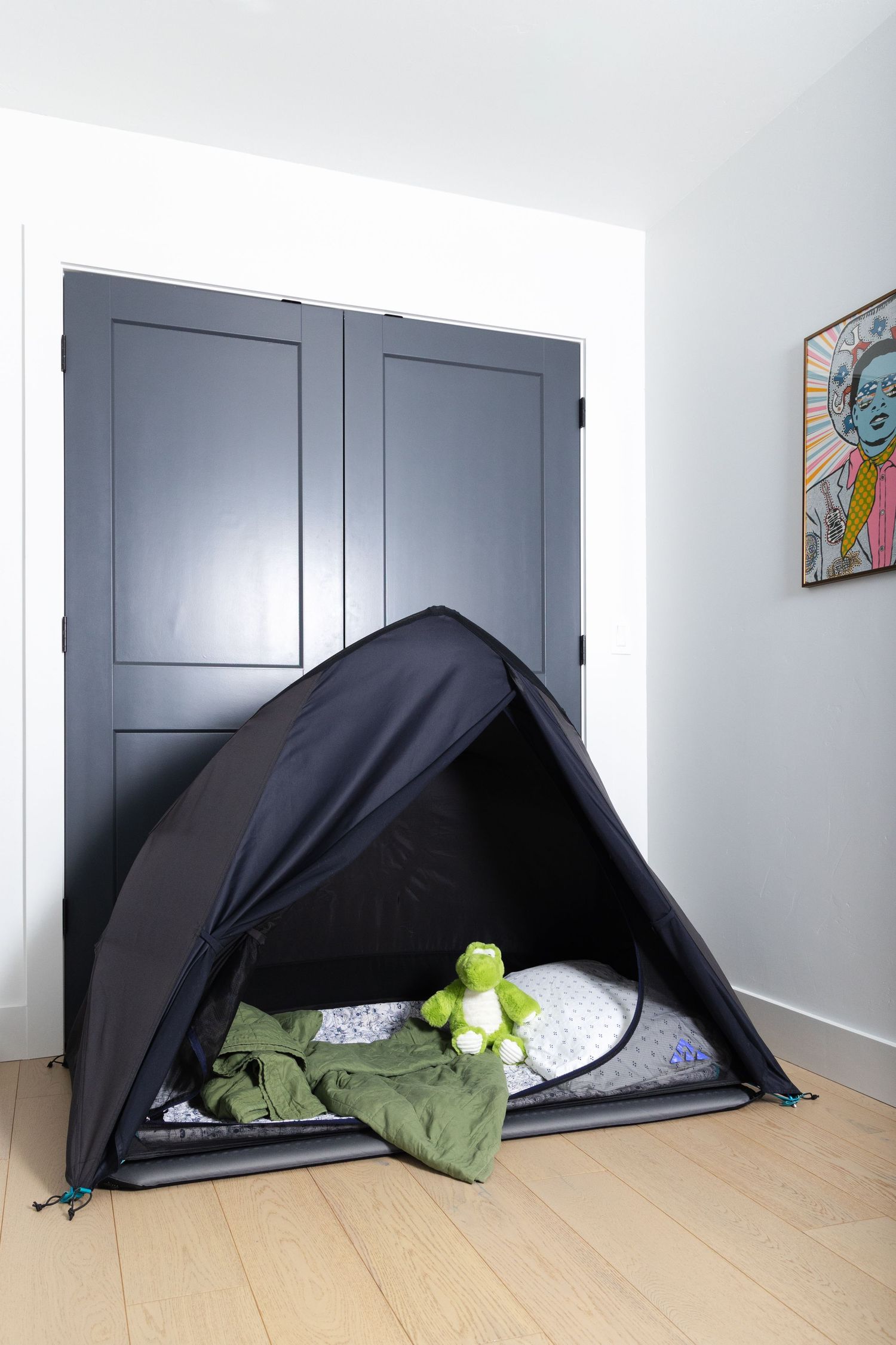 A black tent-like structure is set up against a gray cabinet with a green plush toy peeking out from underneath.