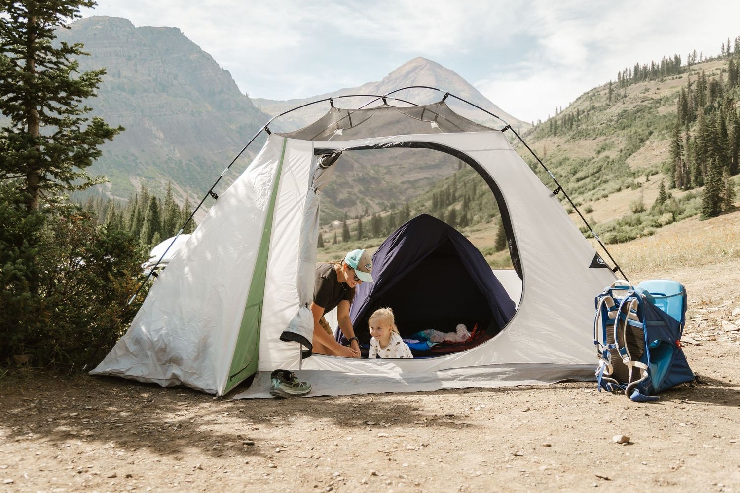A series of camping tents set up along a mountain trail with hiking backpacks and outdoor gear visible.