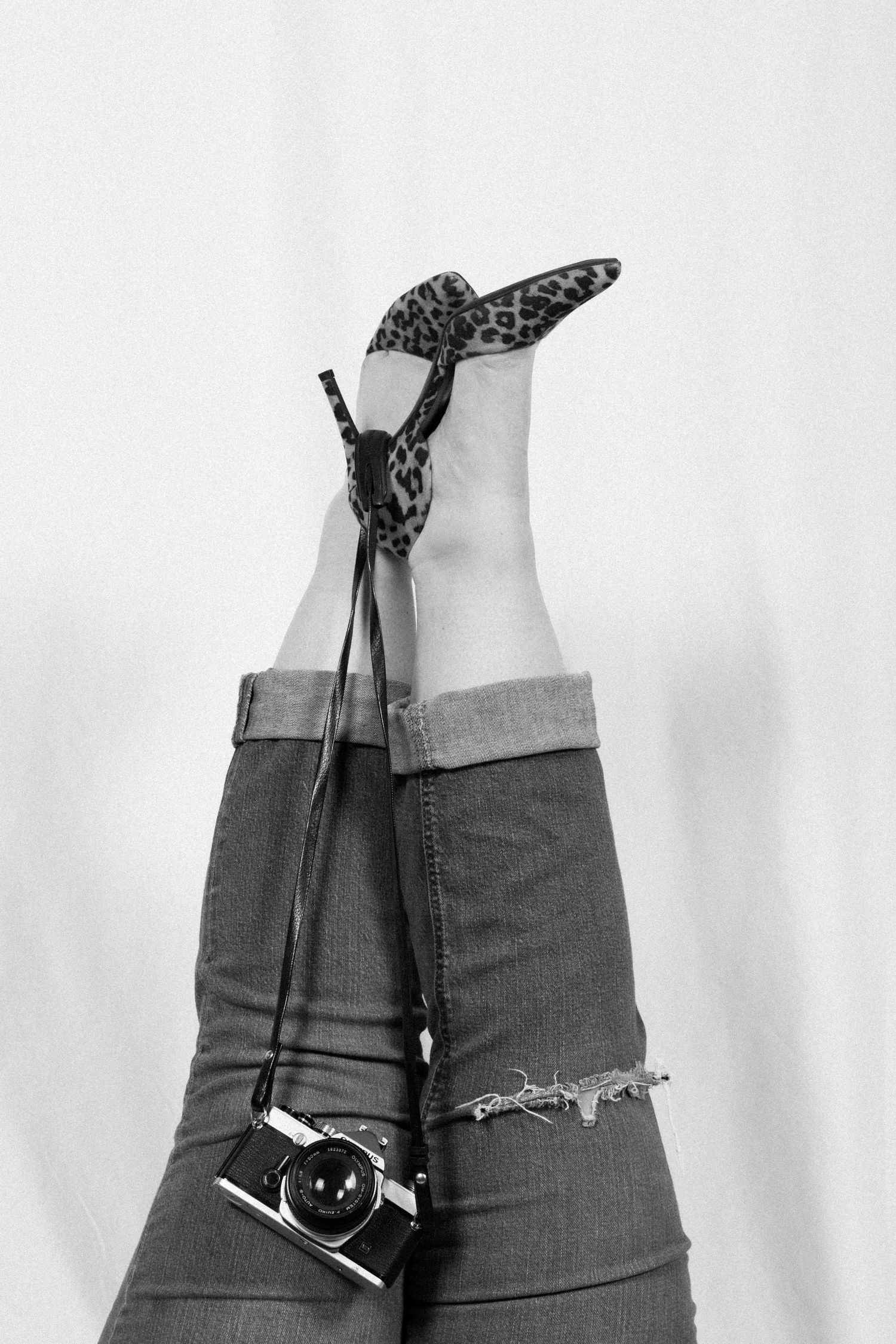 A black butterfly perches delicately on a person's leg wearing distressed denim jeans in a black and white photograph.