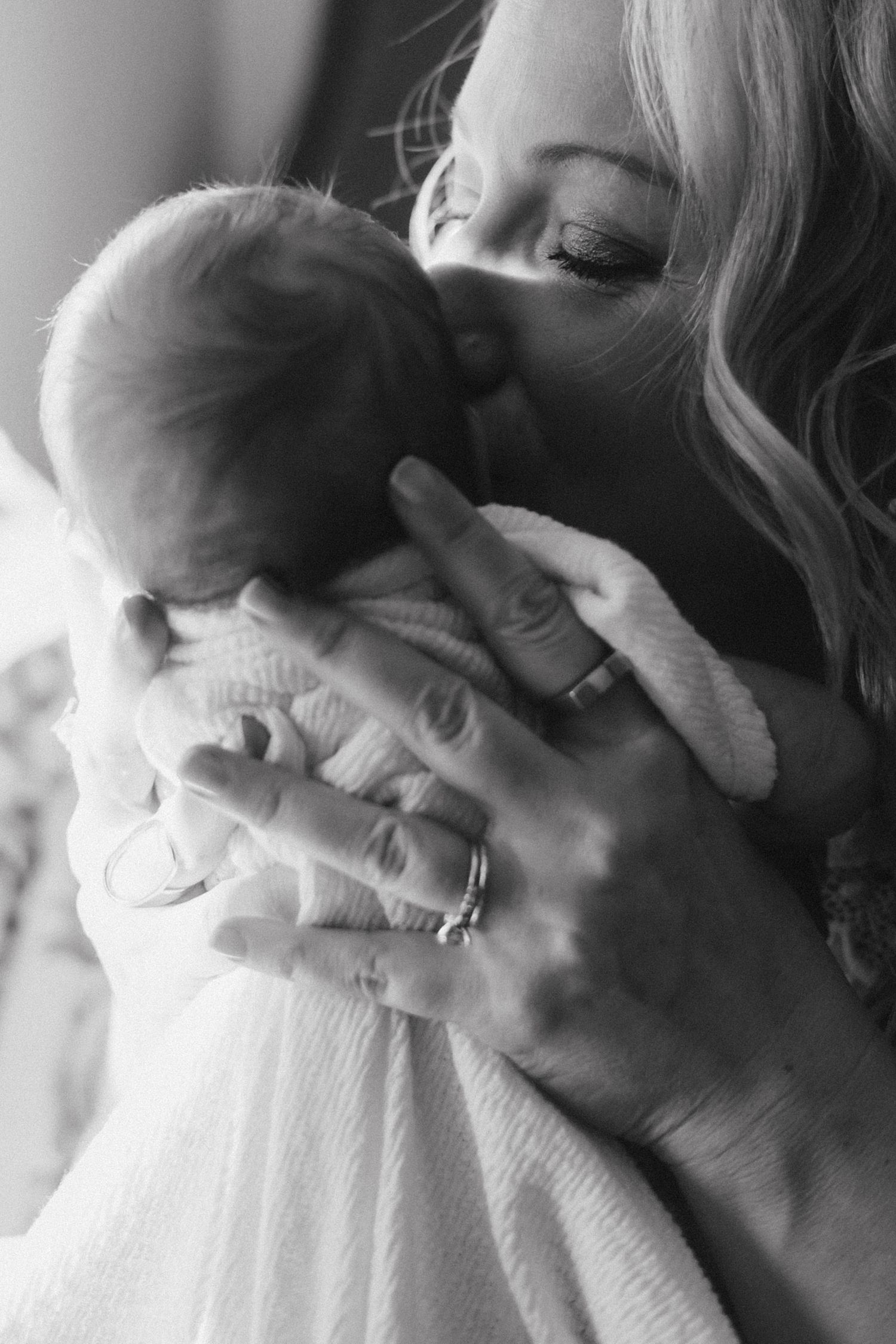 Black and white close-up images showing gentle hands cradling a newborn baby in soft white clothing.