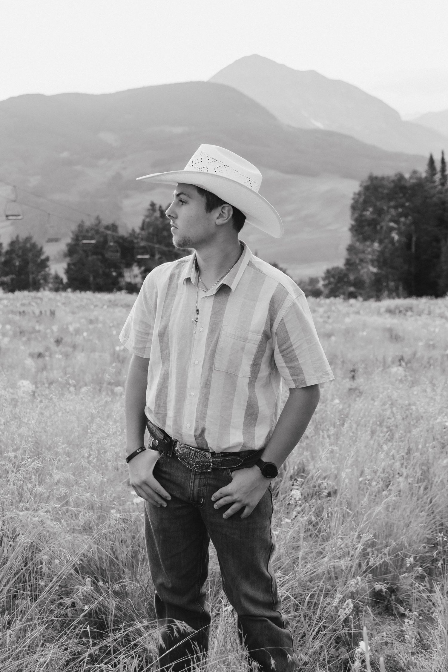A child wearing a cowboy hat and striped shirt poses playfully in a mountain field.