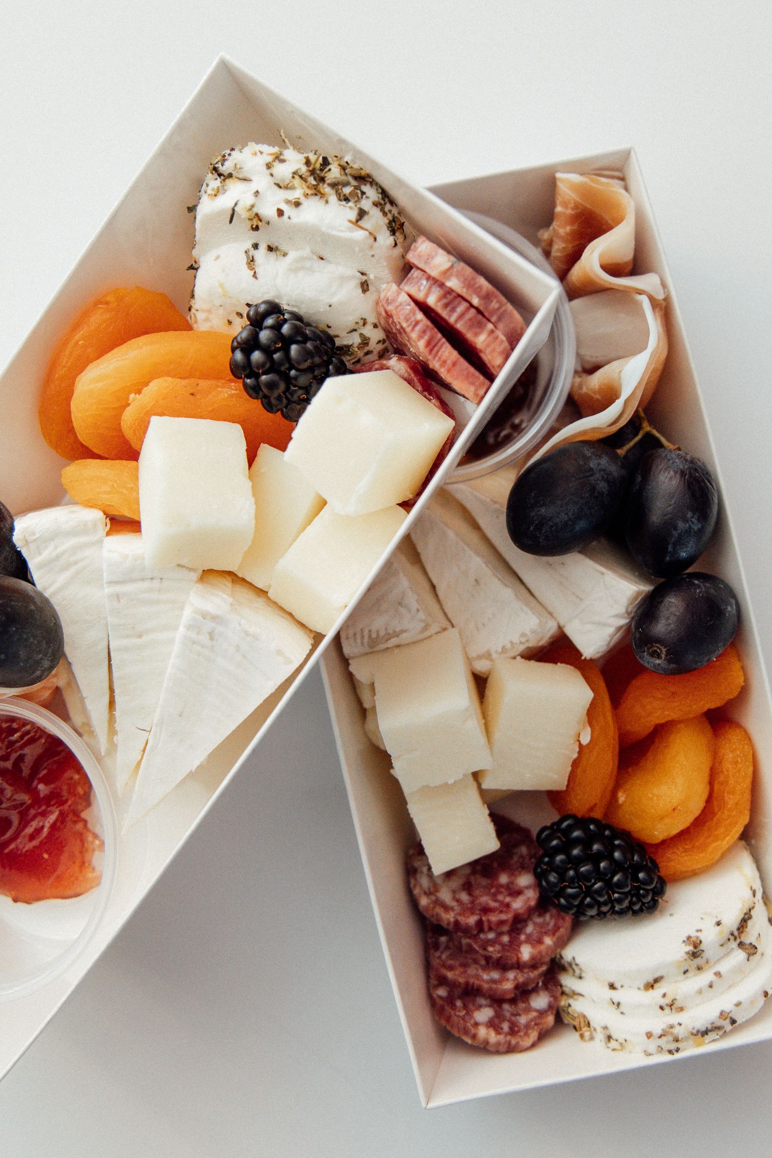 Elegant charcuterie boxes with brie, salami, dried apricots, grapes, and blackberries.