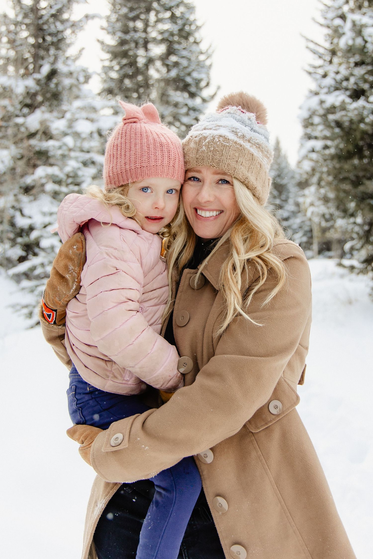 A heartwarming winter scene shows two people in knit hats and coats sharing joyful moments in the snowy forest.