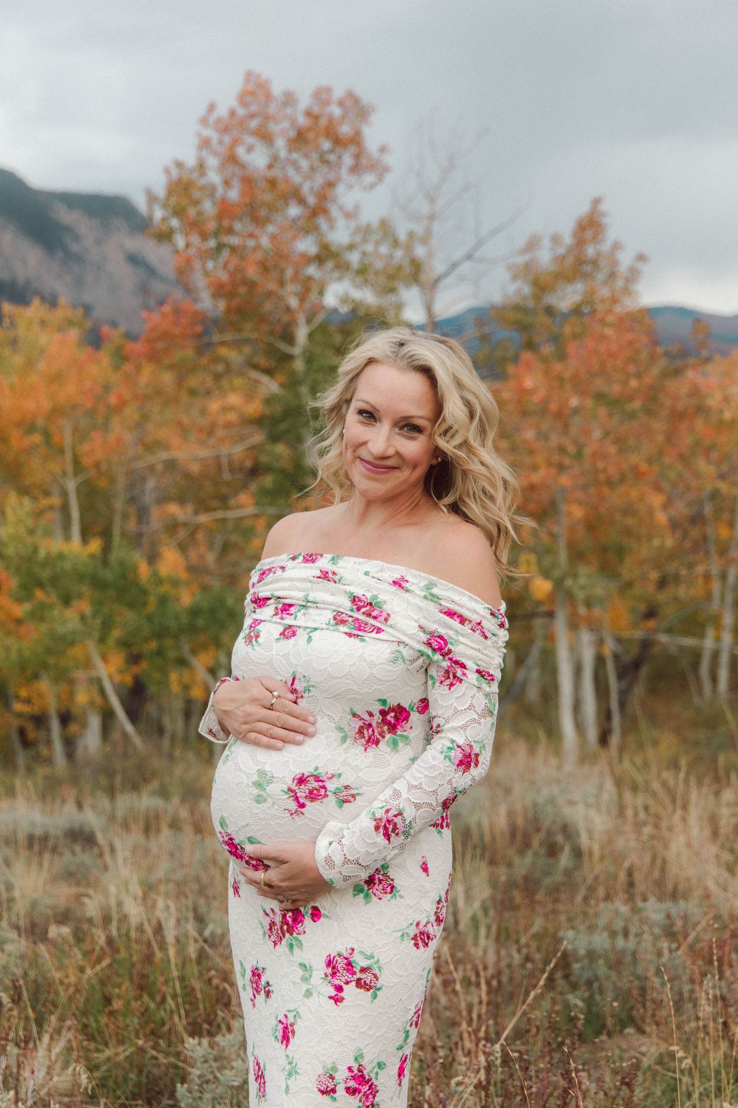 A white and pink floral dress is worn in a scenic fall setting with golden aspen trees.