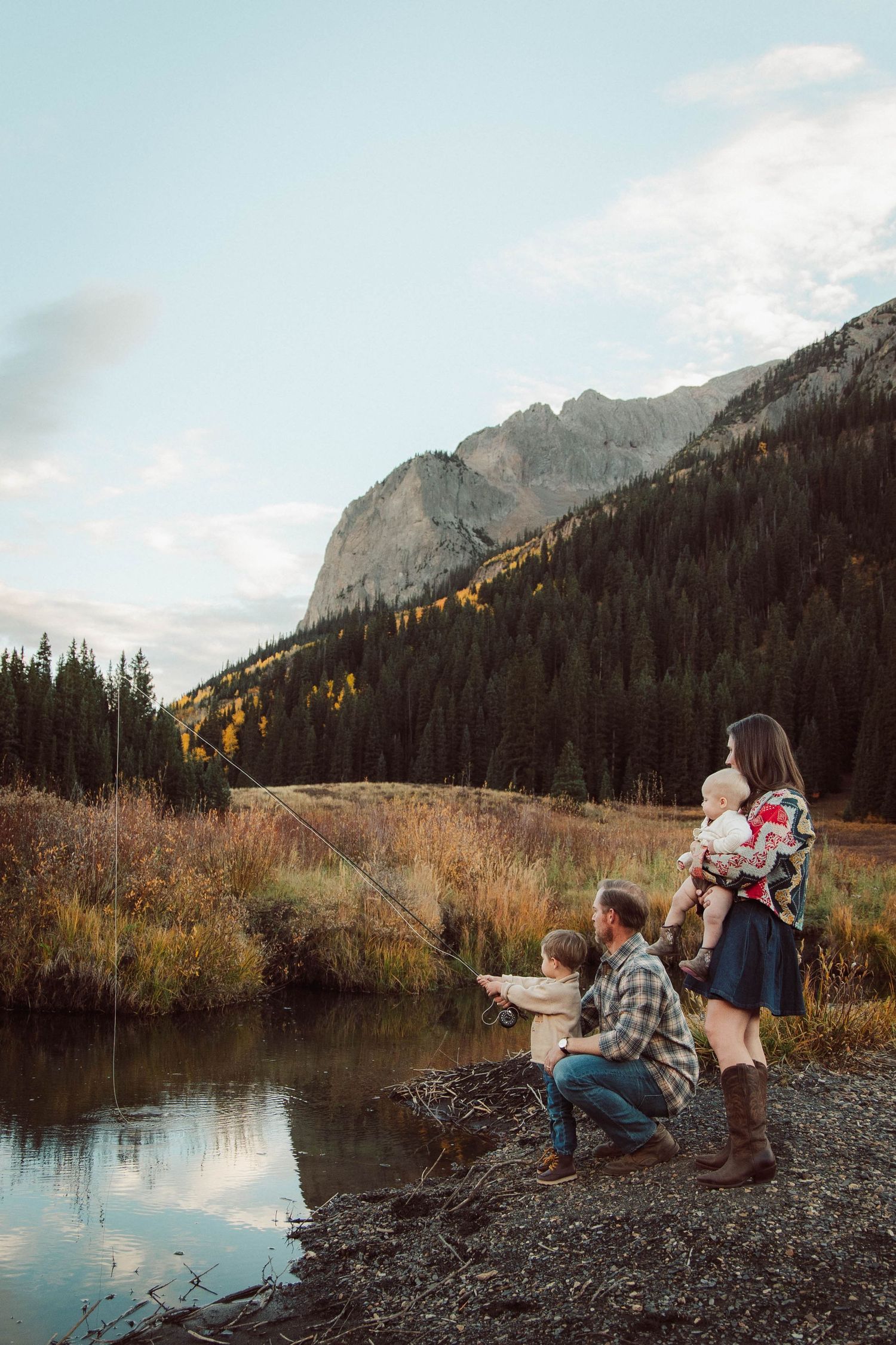 Family relaxing by mountain lake with dramatic peaks and autumn colors in background.