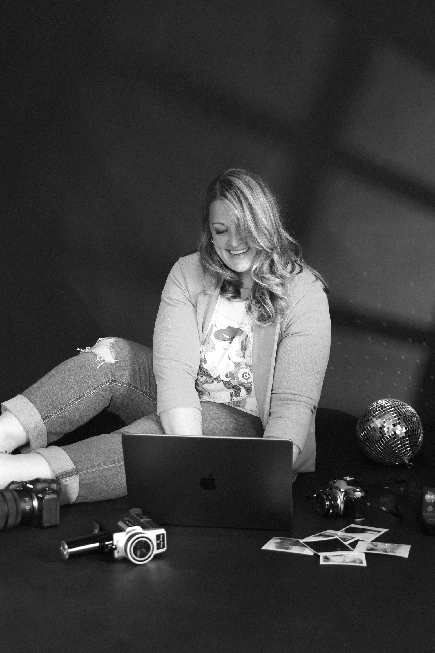 A black and white photo of someone working on a laptop with a vintage camera and decorative items nearby.