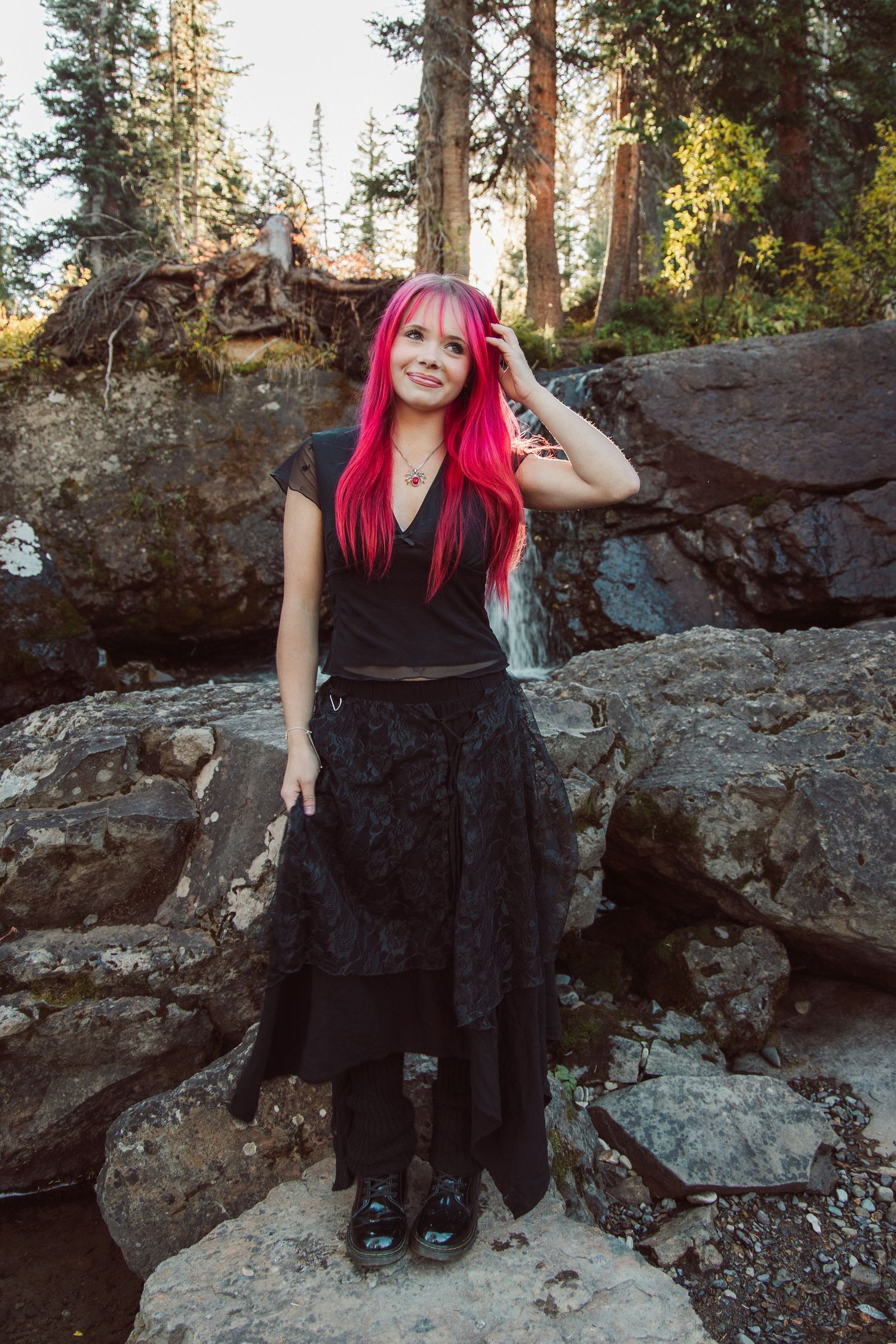 Black dress outfit photographed on rocky mountain terrain with pine trees in background.