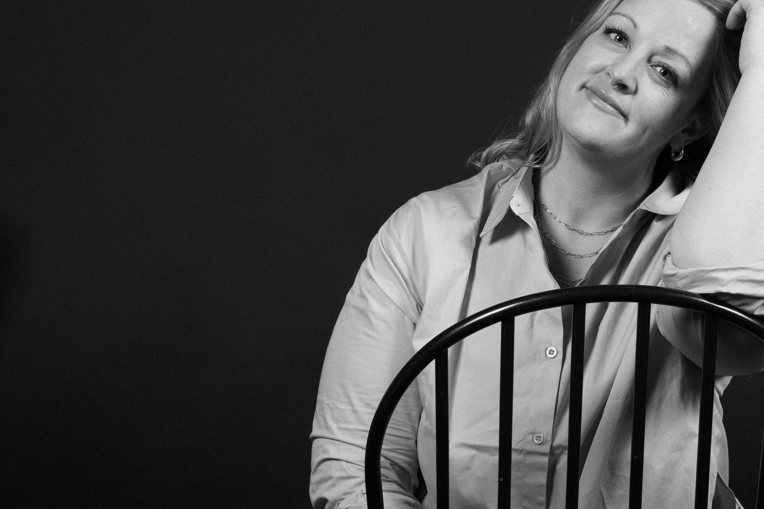Black and white portrait of someone leaning back on a wooden chair with a relaxed expression. Crested Butte