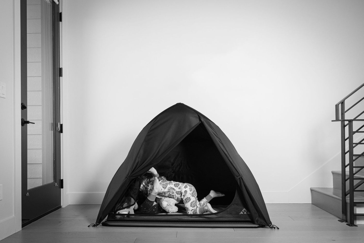 Black and white photograph of camping tents arranged in a row inside an indoor space with white walls.