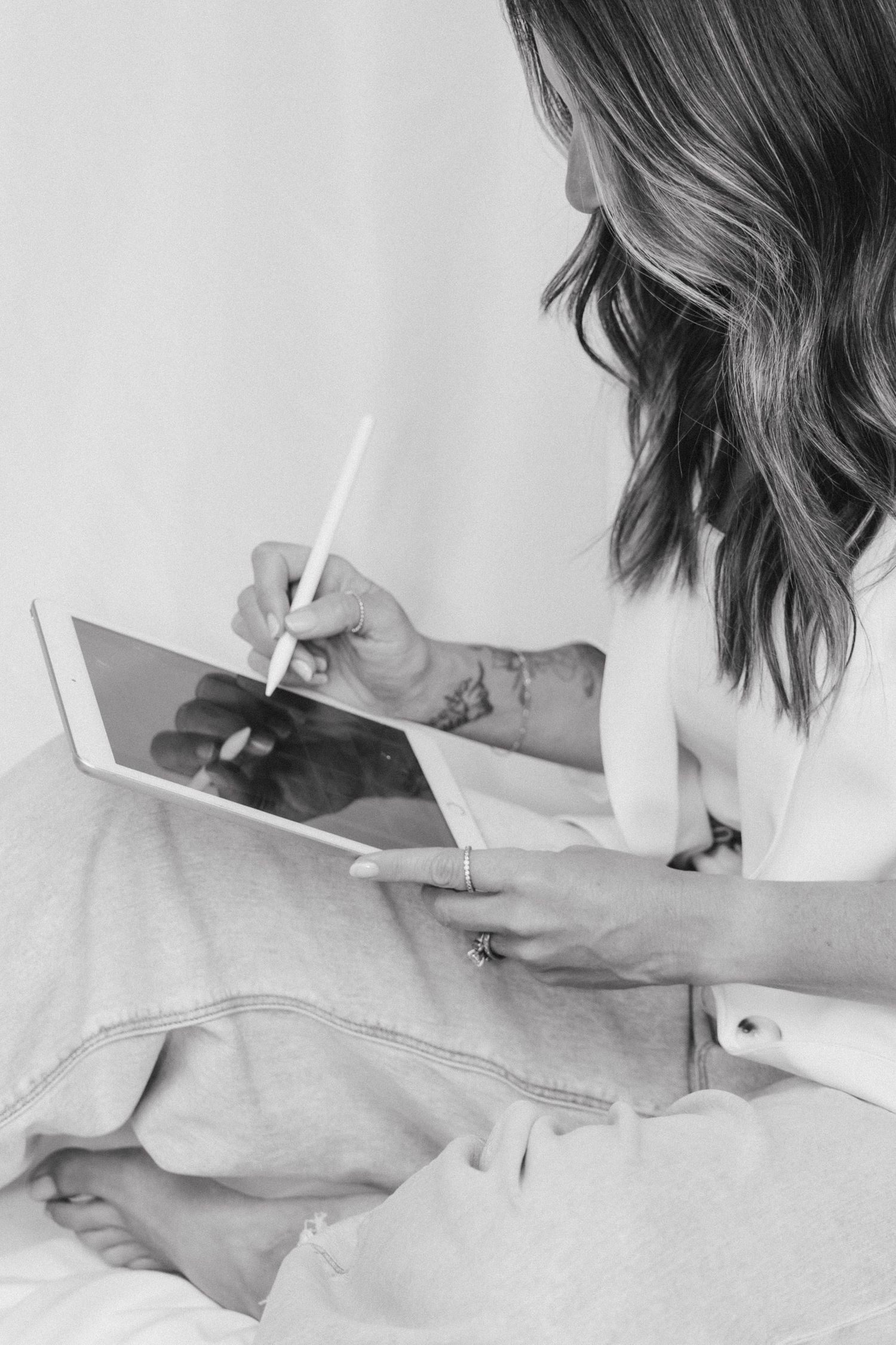 Tattooed woman drawing on a tablet with a stylus while seated.