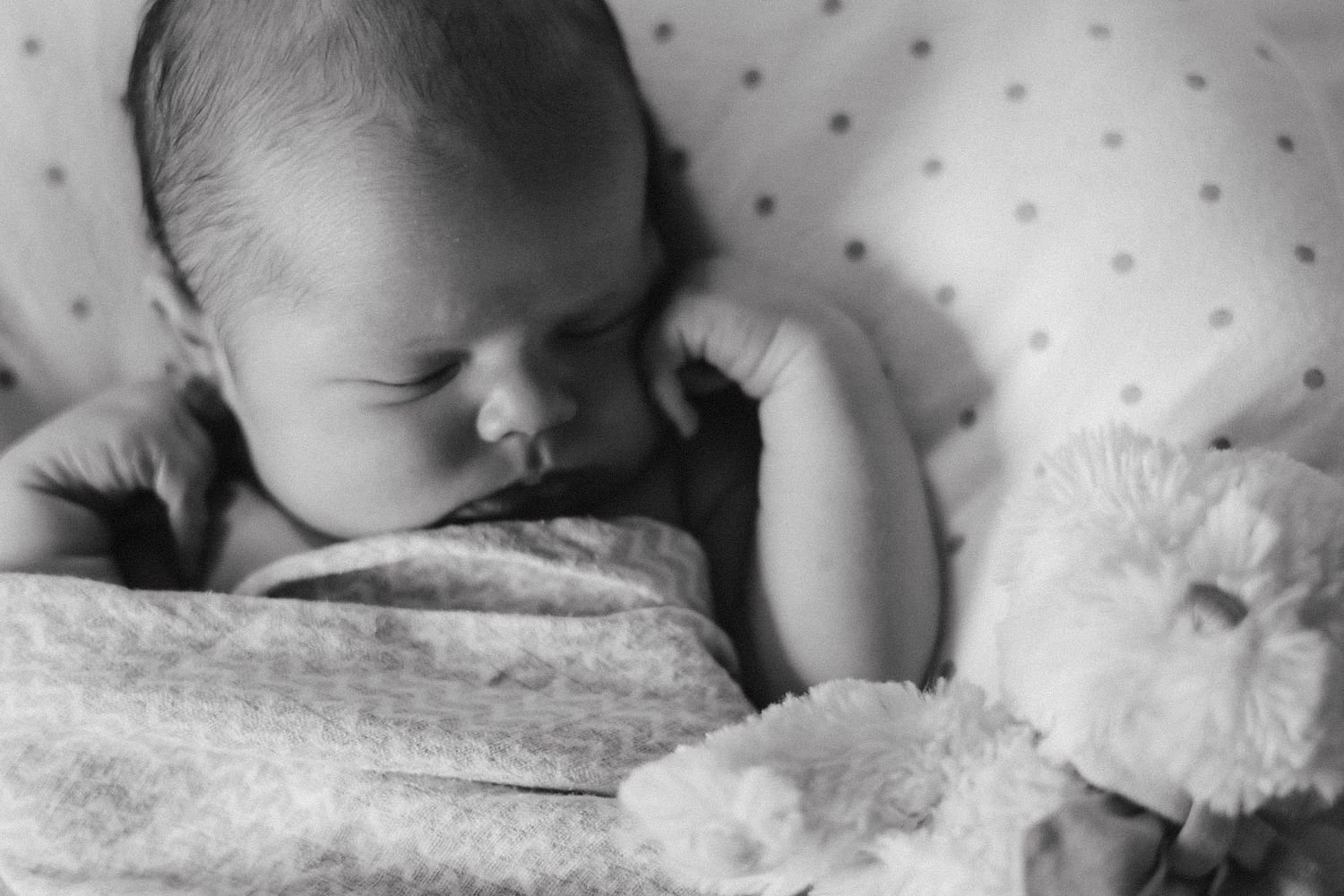 Black and white close-up of a sleeping baby on soft textured bedding.