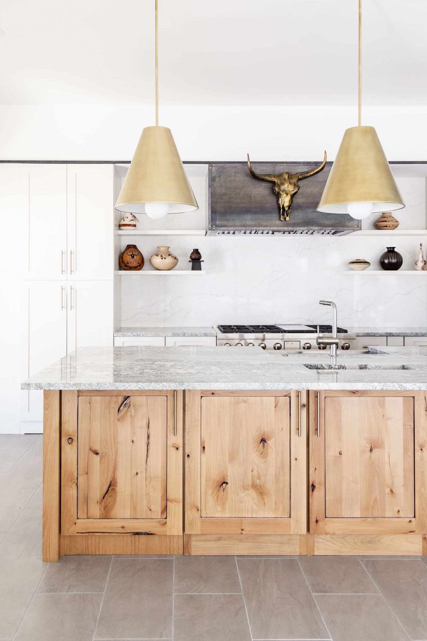 Modern kitchen with natural wood island, marble countertop, gold pendant lights, and decorative open shelving above stainless range.