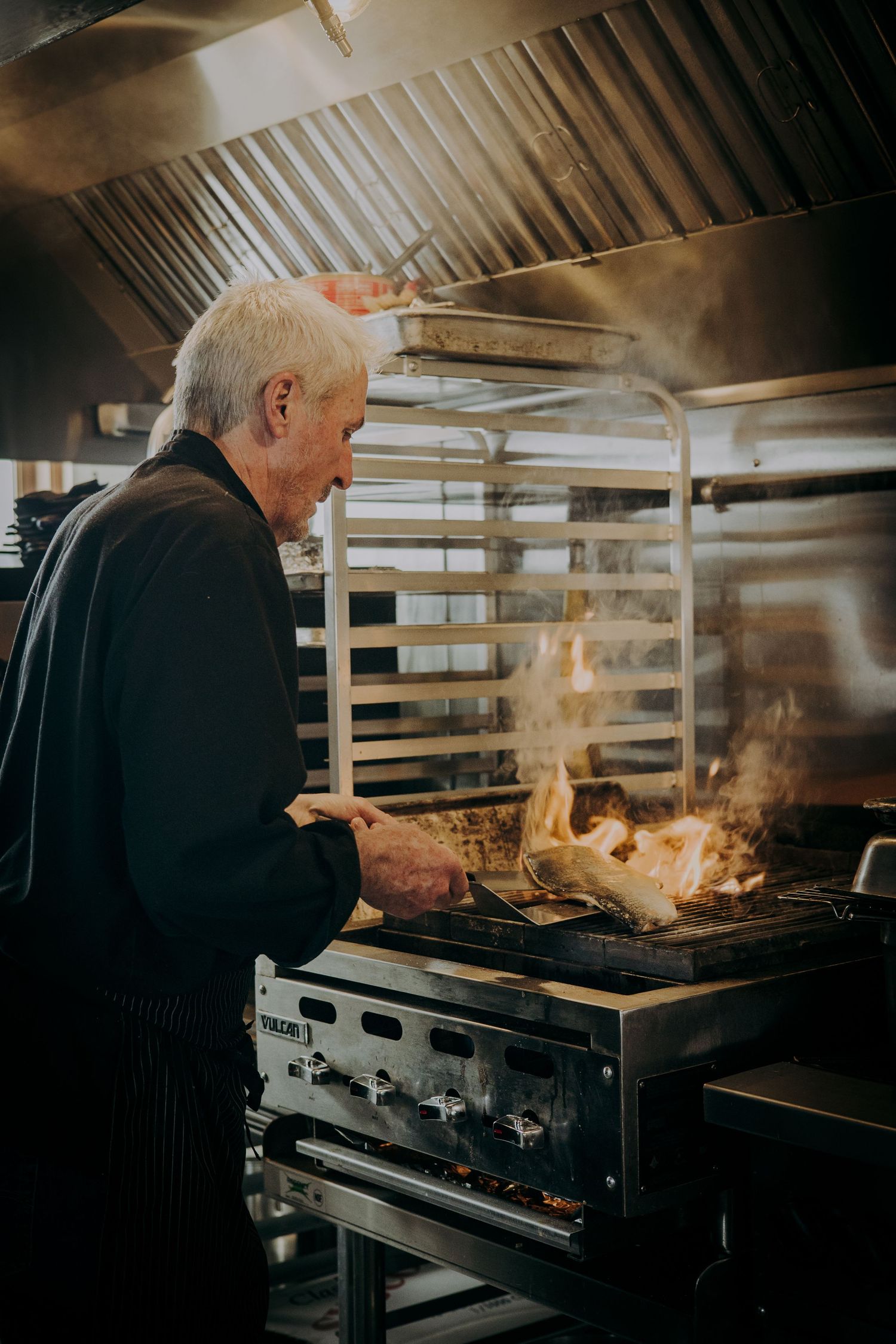Chef cooking with dramatic flames on a commercial grill in a professional kitchen.